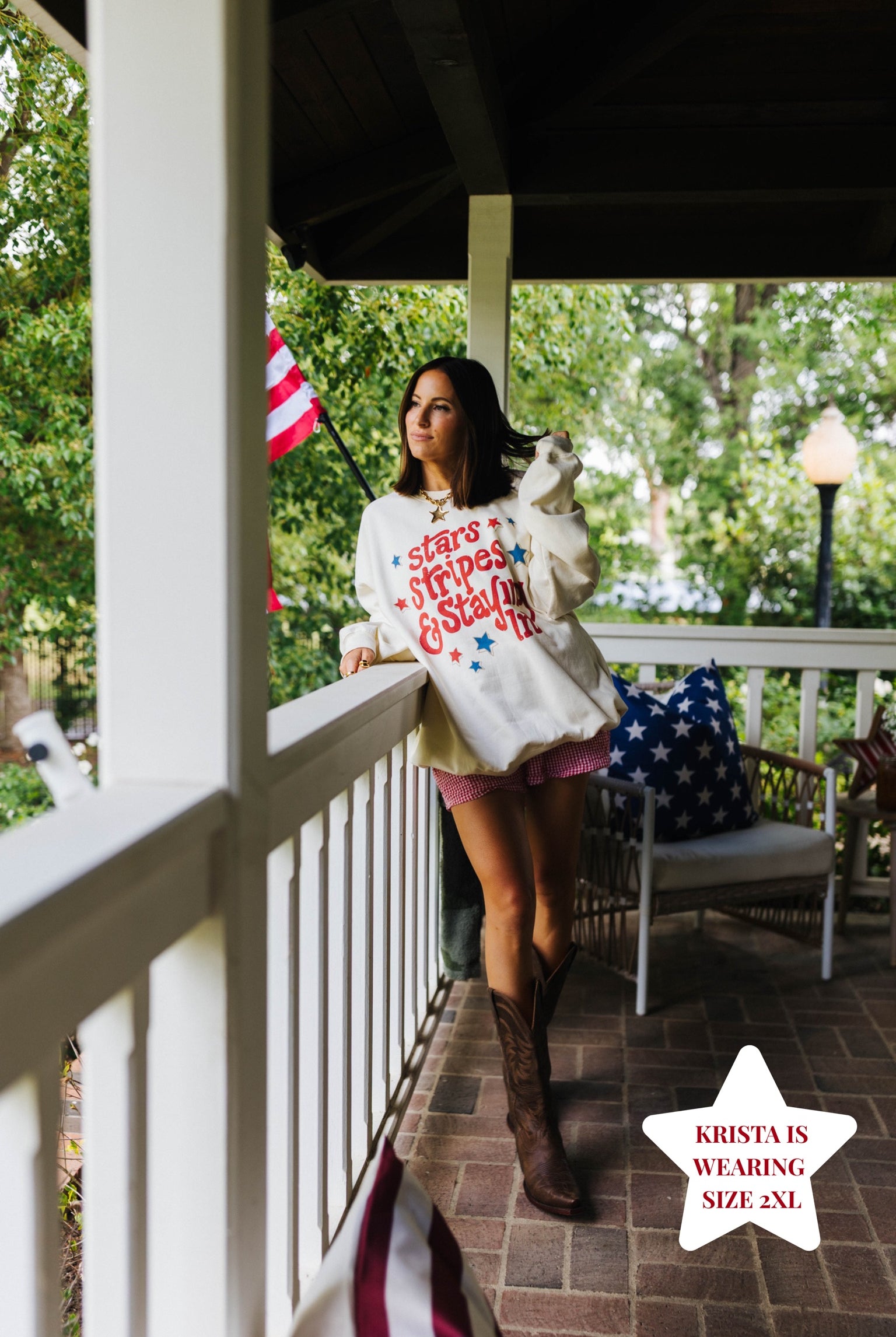 person posing in the sweatshirt on a frotn porch with white railing