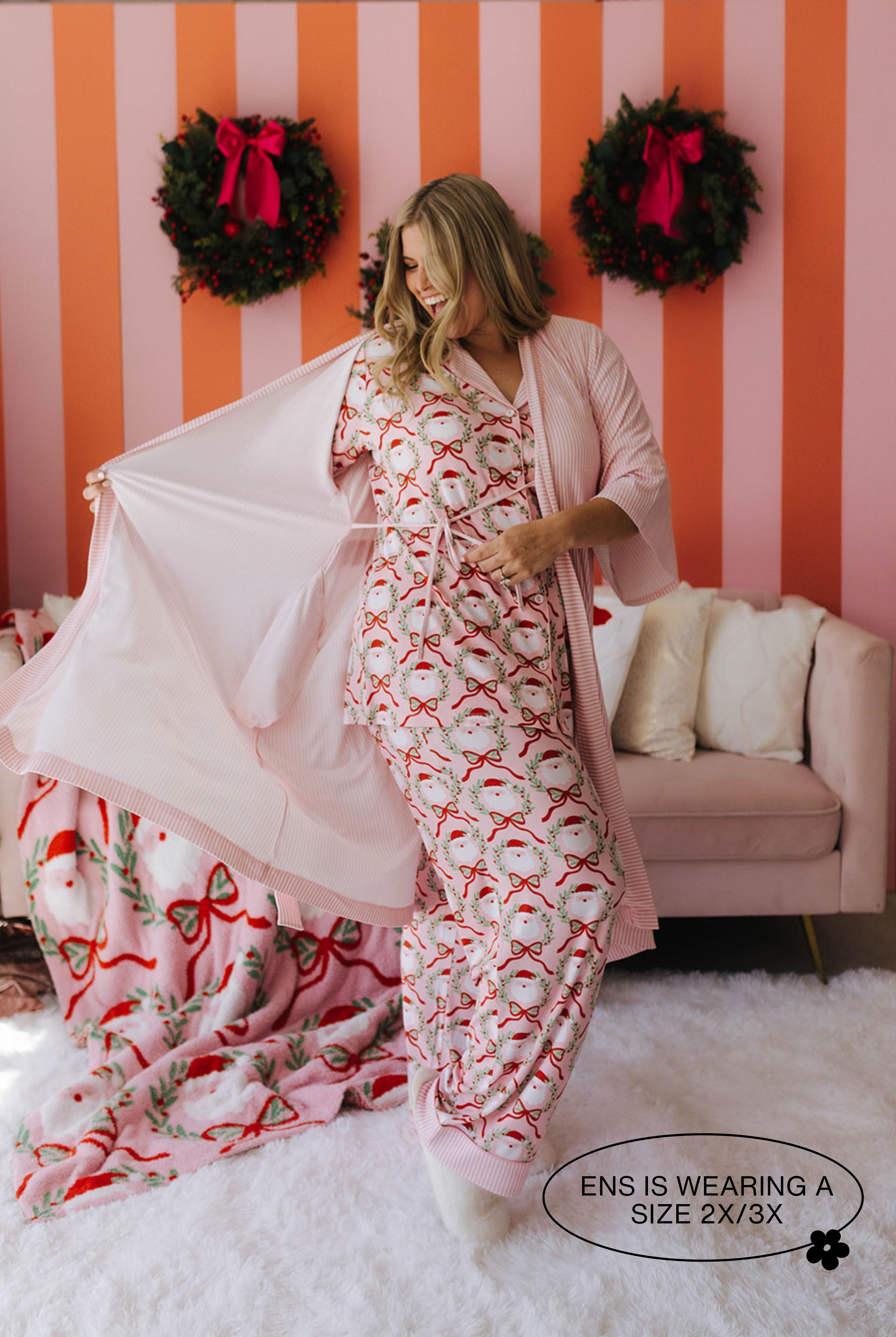 Woman wearing a festive pajama set with matching robe in a room with striped walls and wreaths.