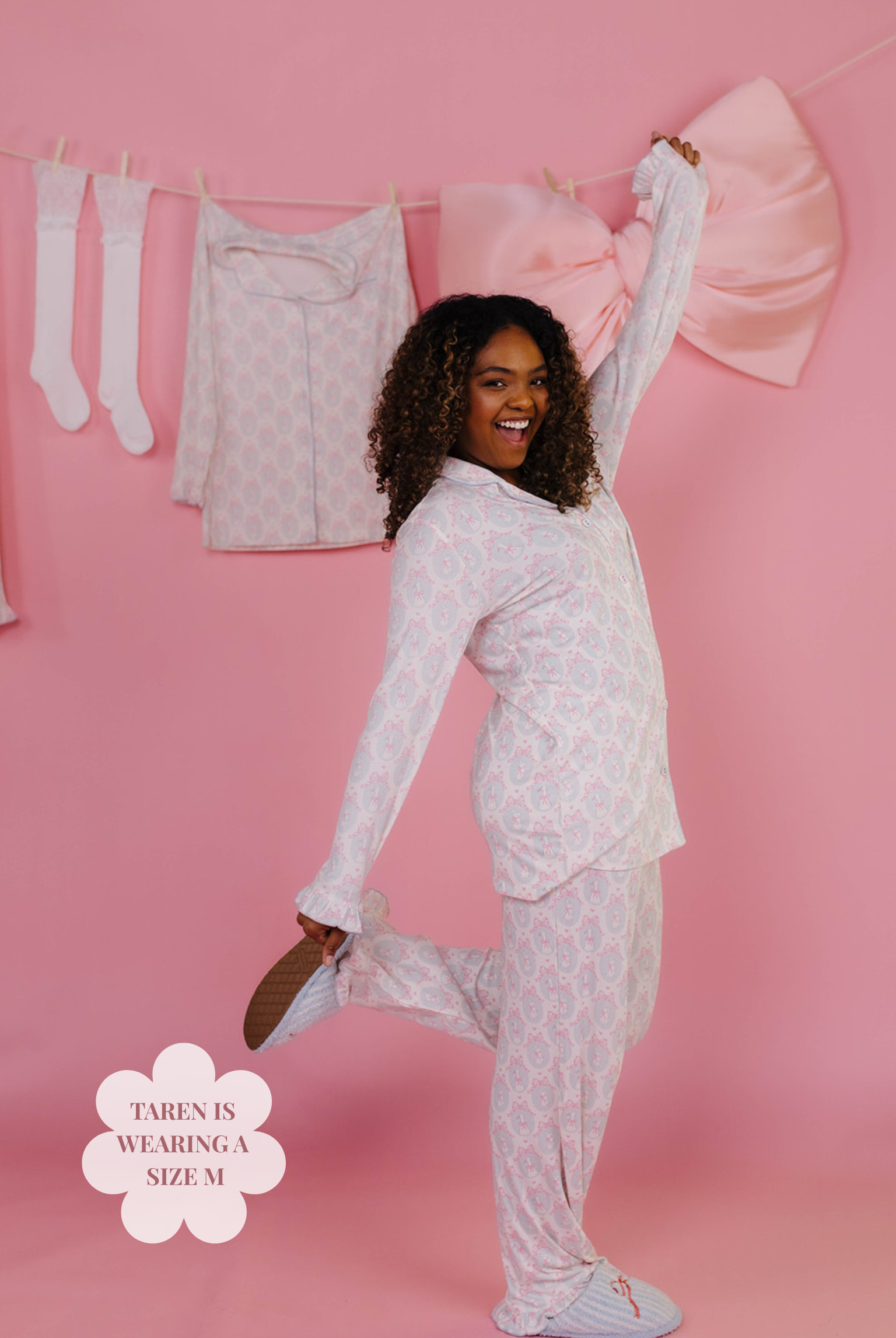 Woman wearing a white pajama set on a pink background with laundry in the background.