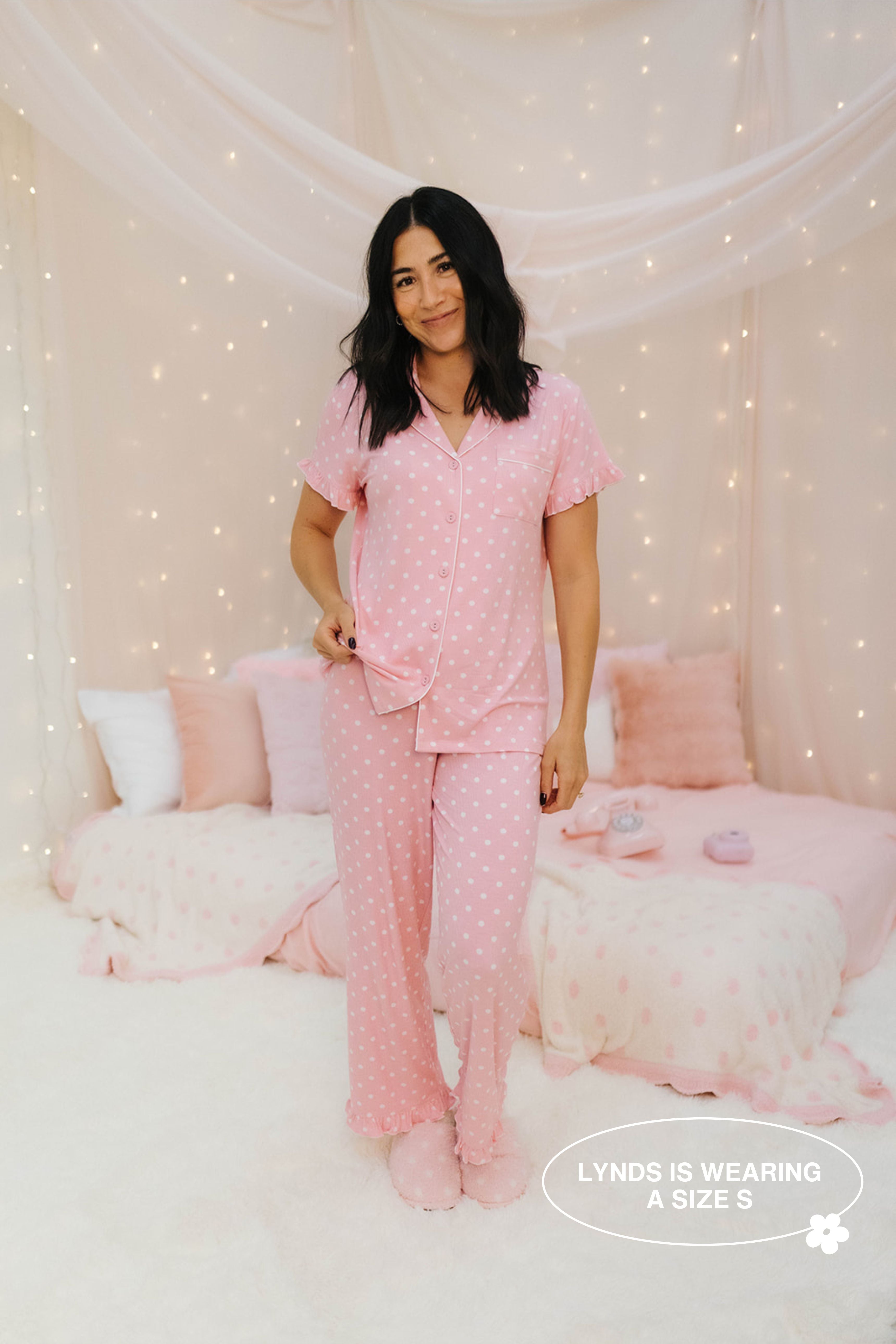 Woman wearing pink pajamas in a cozy bedroom setting with soft lighting.