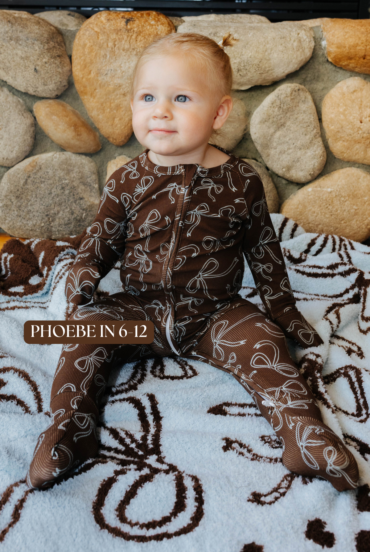 Sizing photo: Phoebe in 6-12 months wearing brown bow print baby zip pajamas.