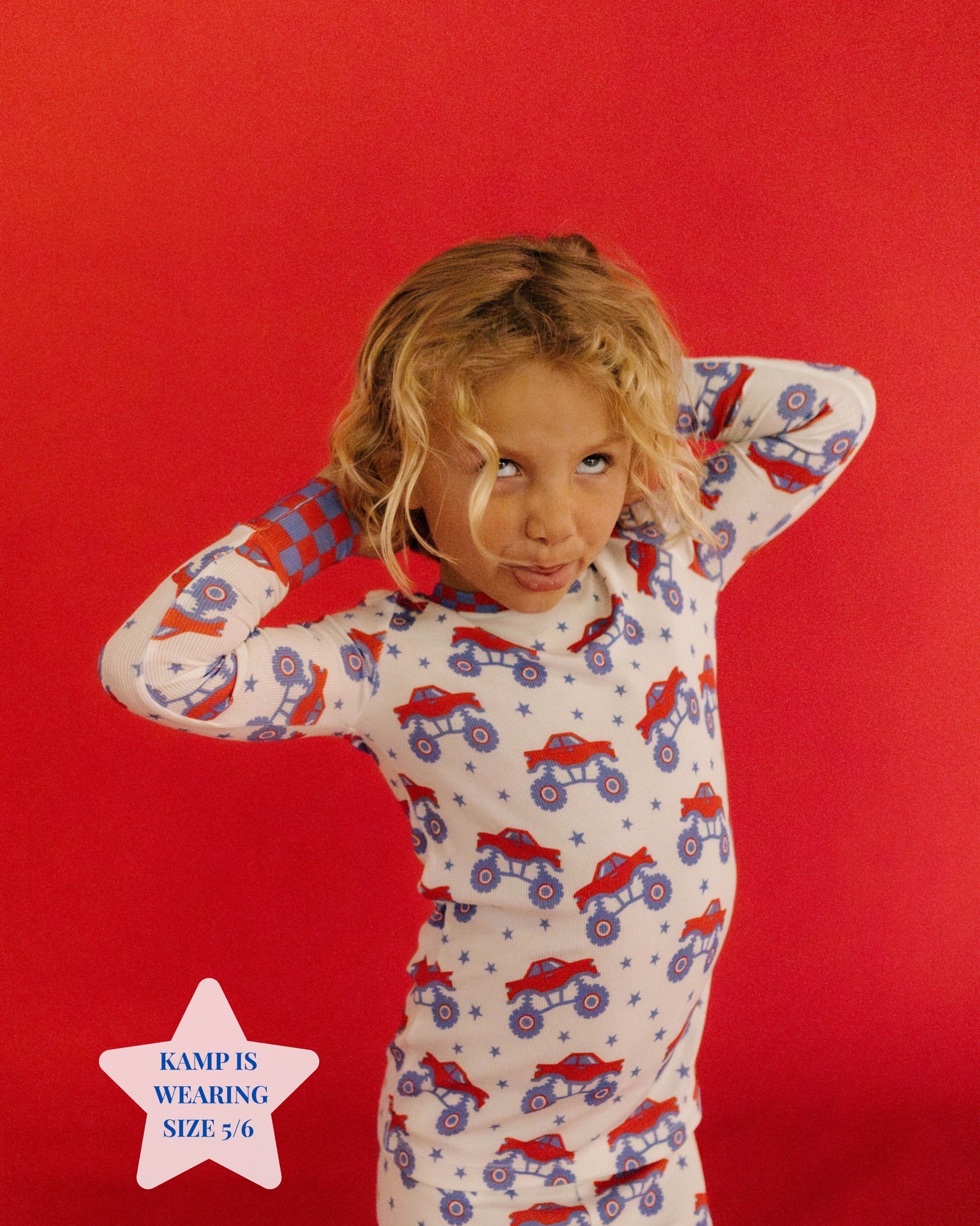 Child wearing pajamas with truck pattern on a red background