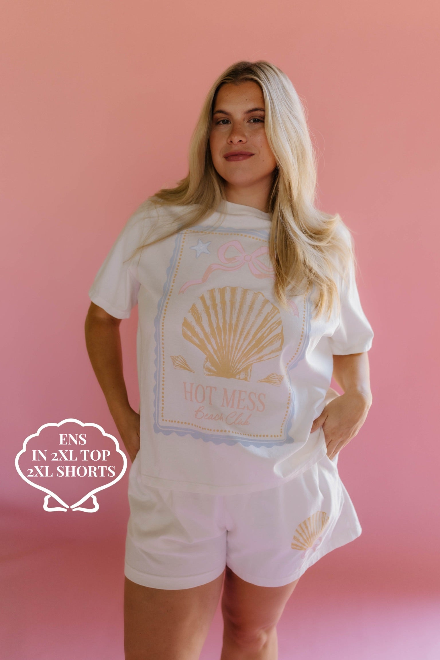 Woman wearing a white t-shirt with a shell graphic and shorts on a pink background size 2xl