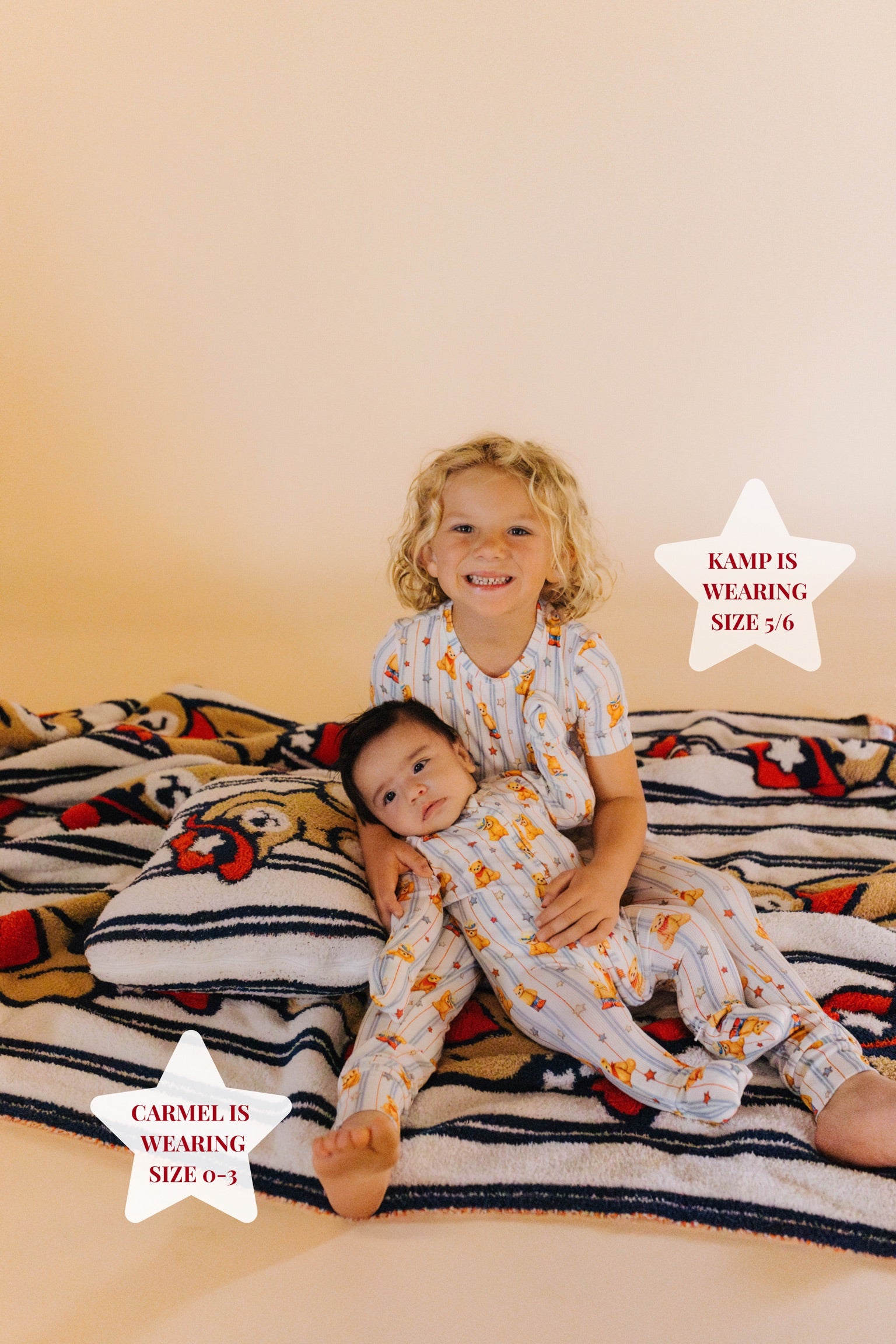 Two children in matching pajamas sitting on a colorful blanket.