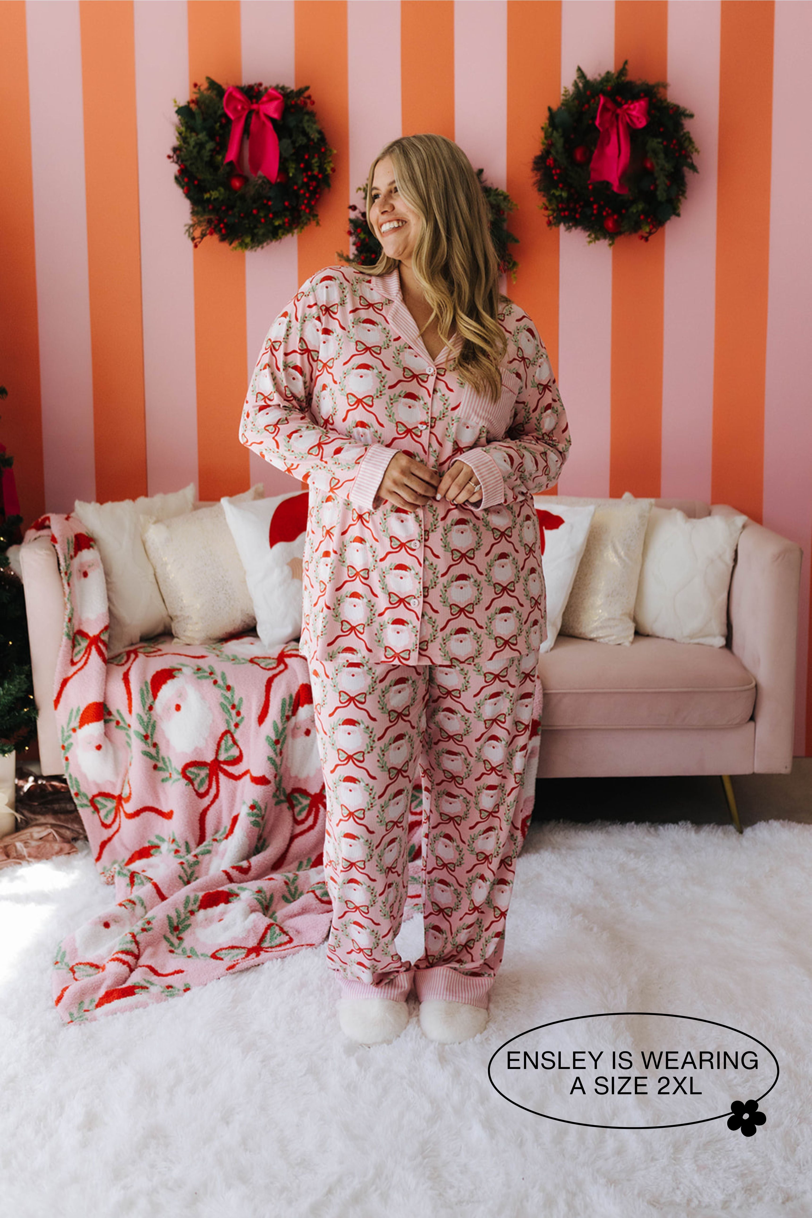 Woman wearing a festive pajama set in a decorated room with wreaths on a striped wall.