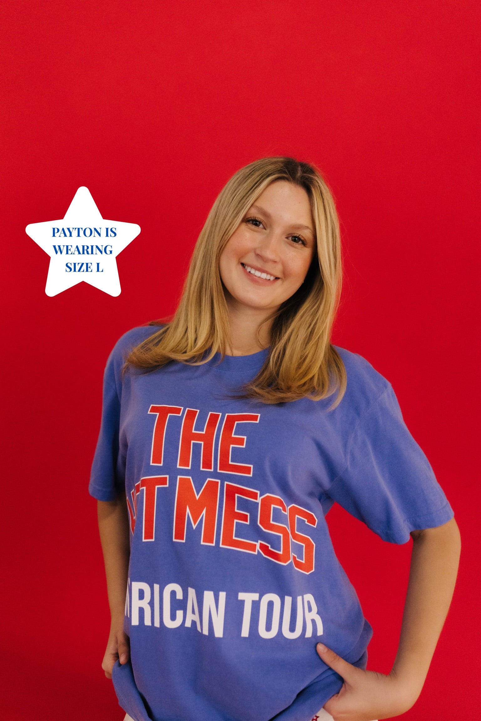 girl standing in front of a plain red backgroud showing the hot mess american tour tee