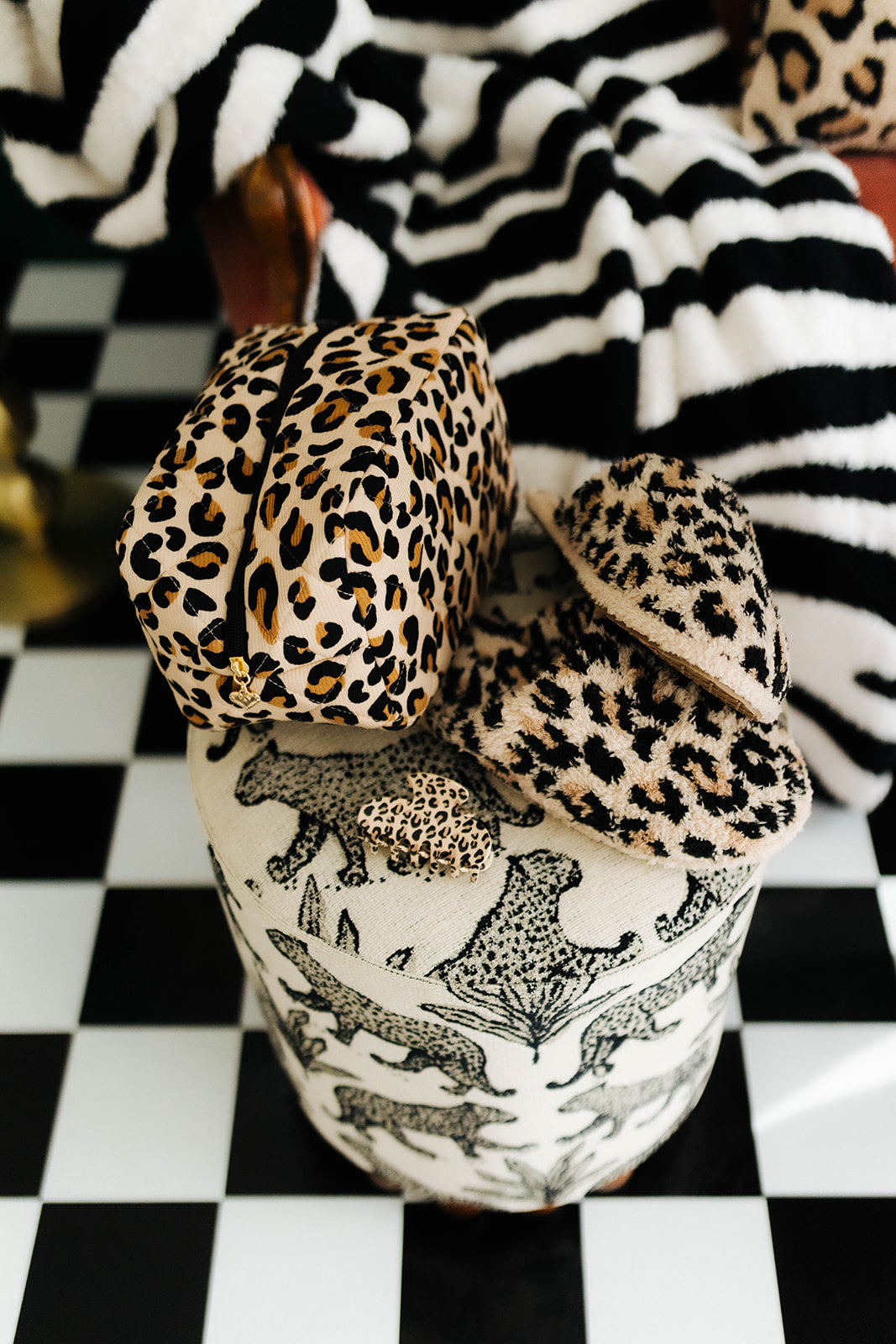 Leopard print slippers and cosmetic bag sitting on an animal print stool with a checkered floor