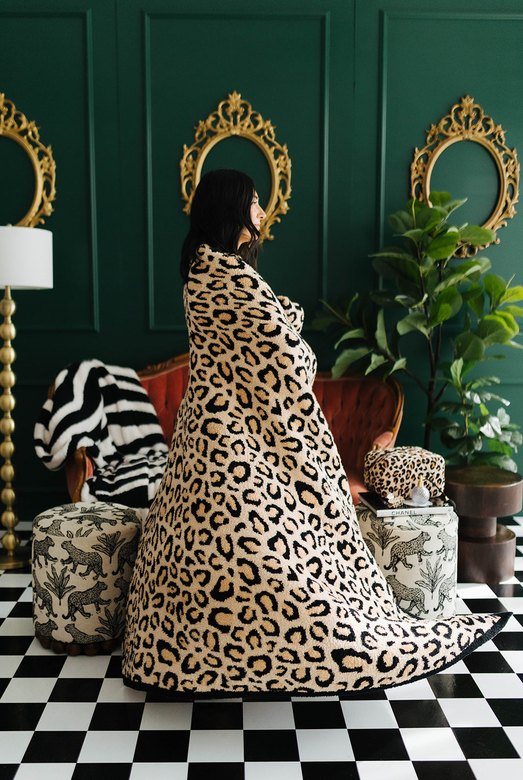 Person wrapped in a leopard print blanket in a stylish room with green walls, gold mirrors, and patterned furniture.