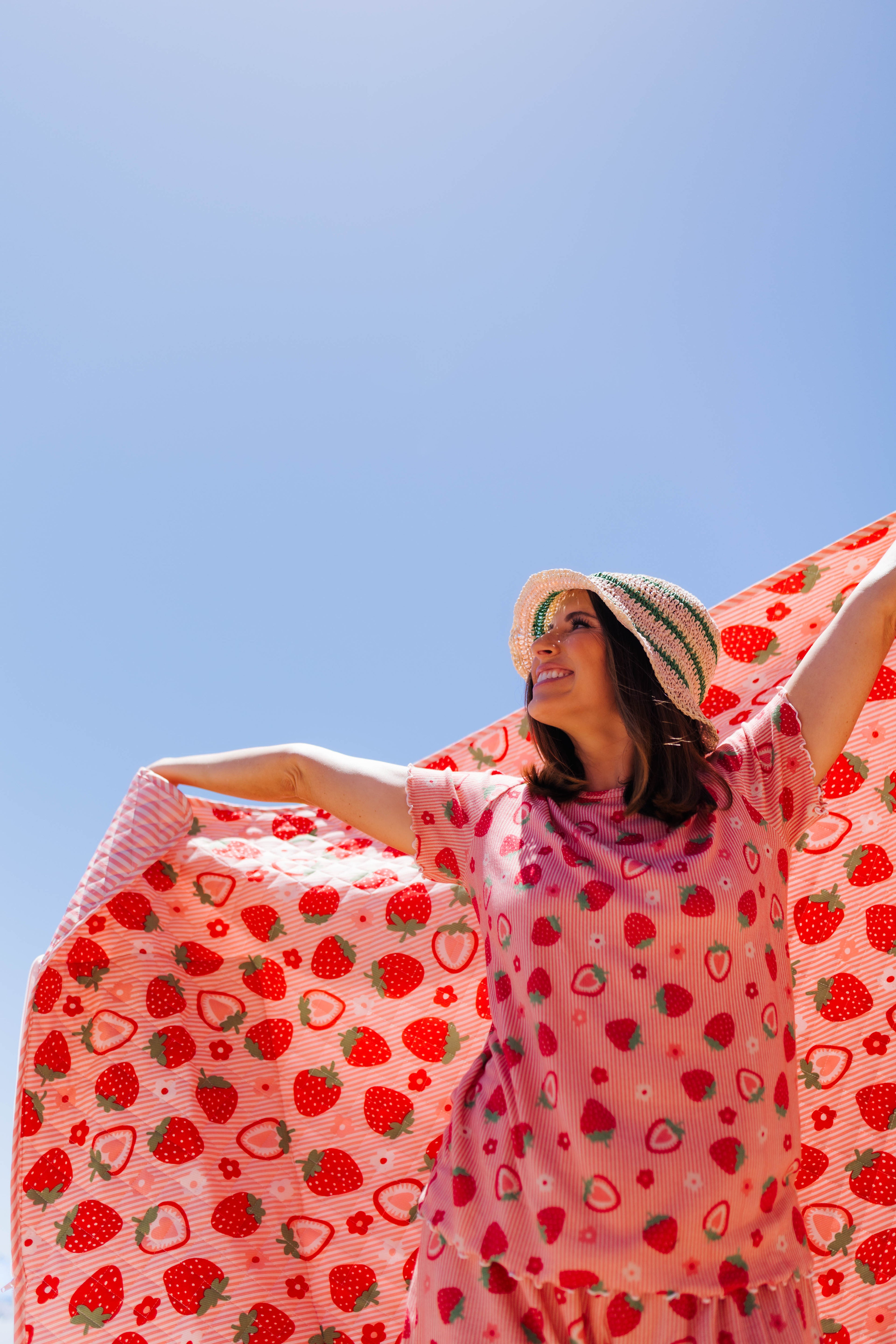 Krista holding the strabwerry outdoor quillow into the air with her matching strawberry pjs