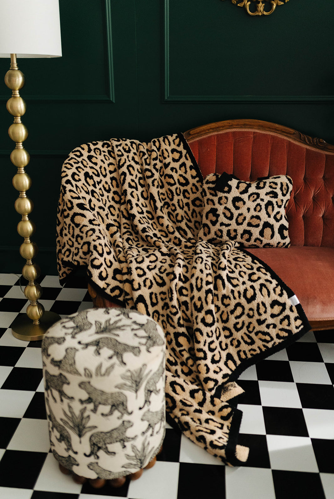 Leopard print blanket draped over a red sofa in a room with a checkered floor and lamp.