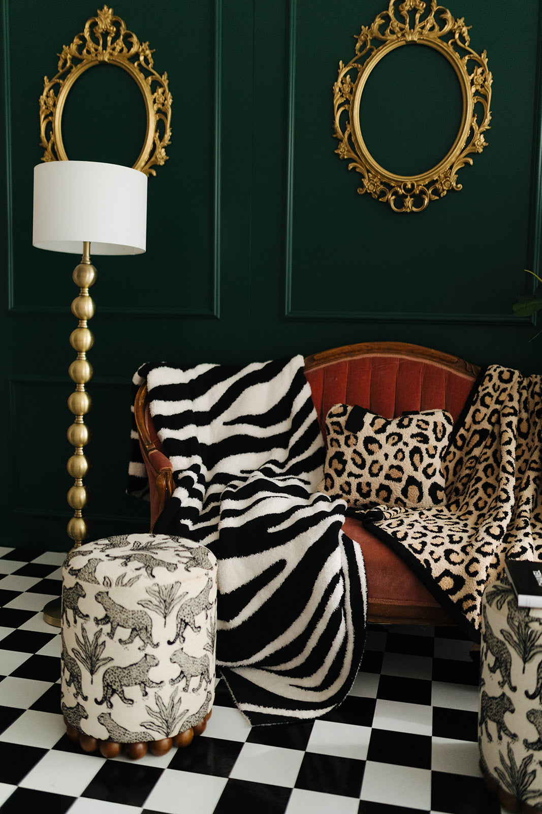 Living room with zebra print blanket, leopard print pillow, and gold-framed mirrors on a dark green wall.