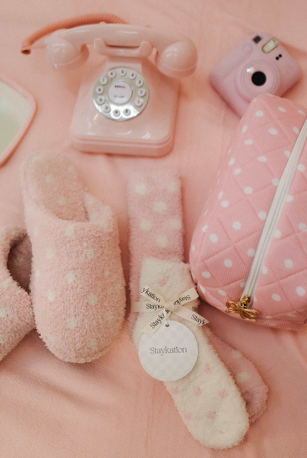 Collection of pink and white items including a phone, camera, slippers, and pouch on a pink background.