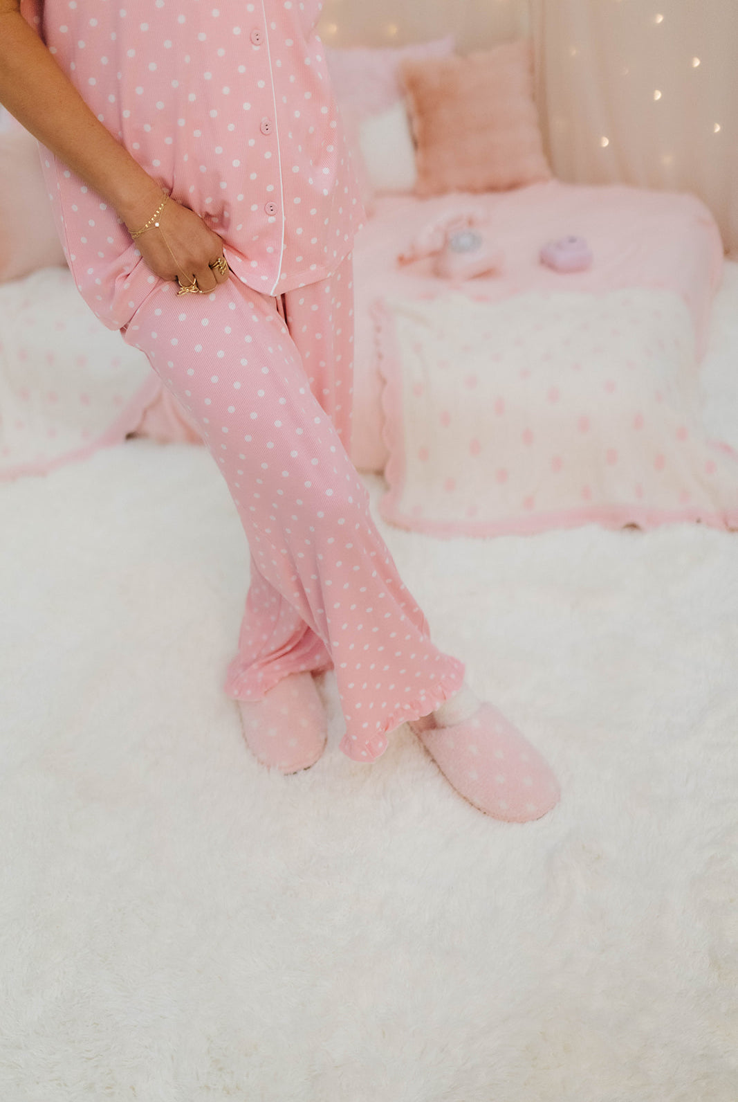 Person wearing pink polka dot pajamas sitting on a white bed with pink polka dot slippers