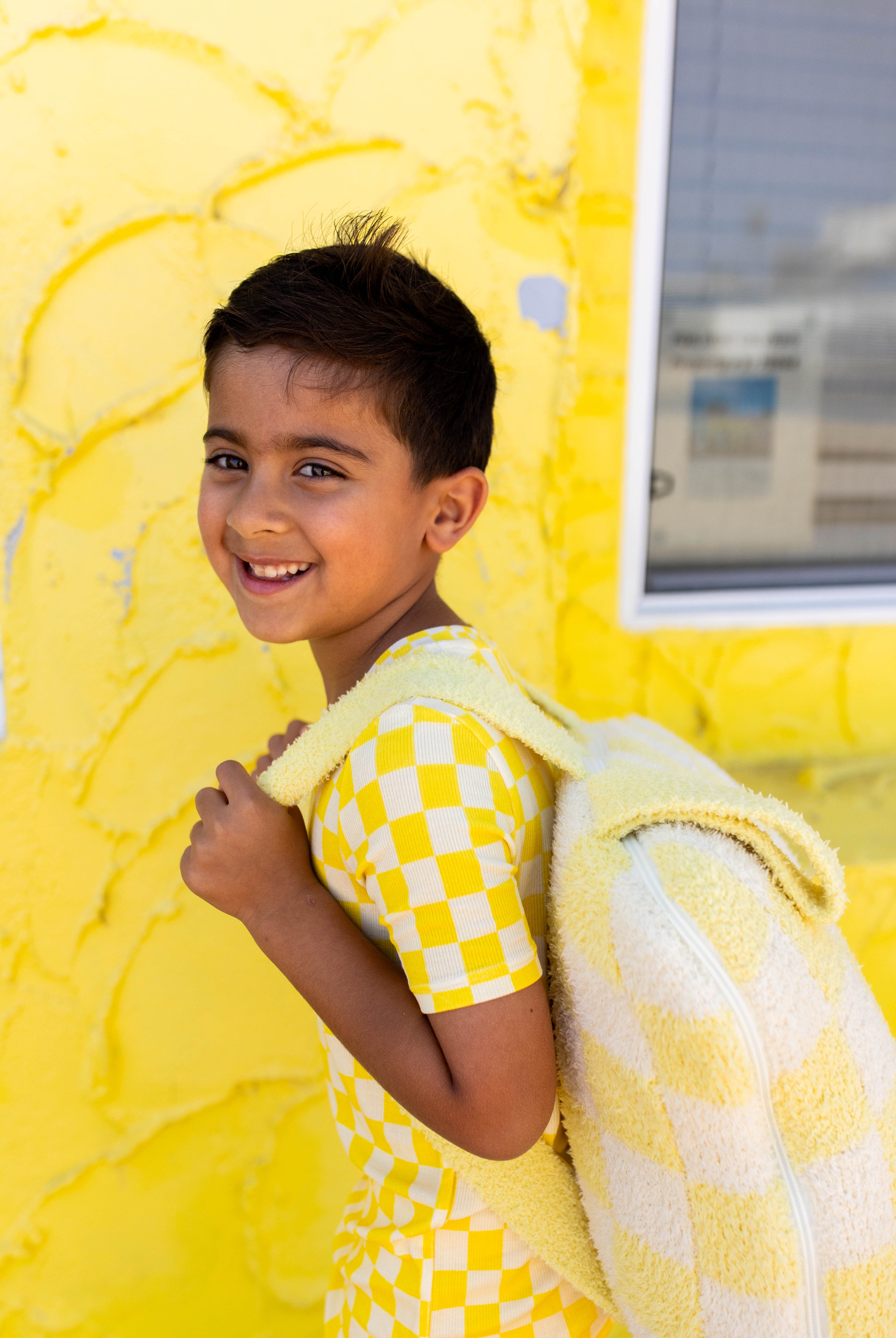 A young boy smiling and looking back over his shoulder with the backpack quillow on him.
