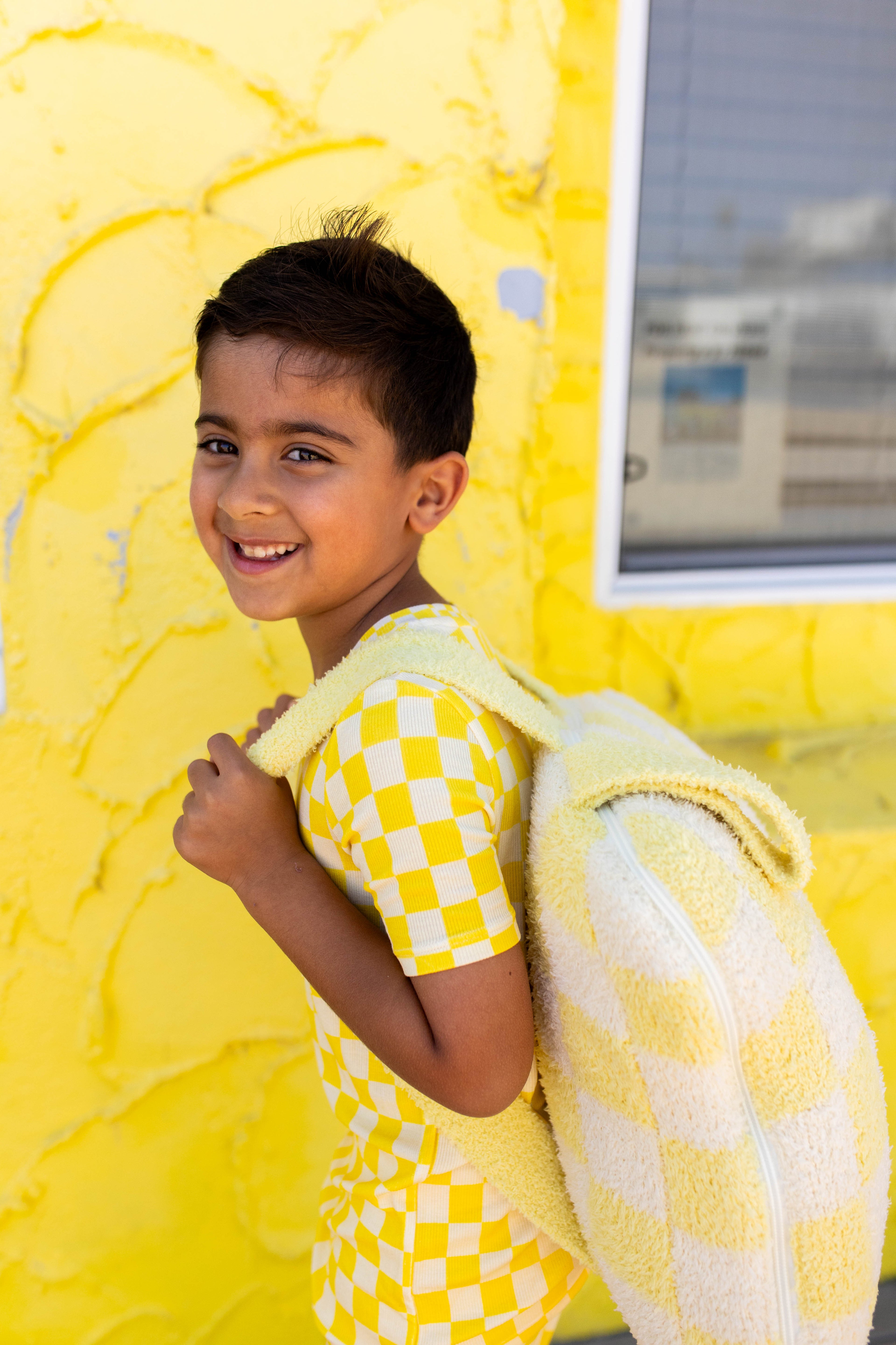 A young boy smiling and looking back over his shoulder with the backpack quillow on him.