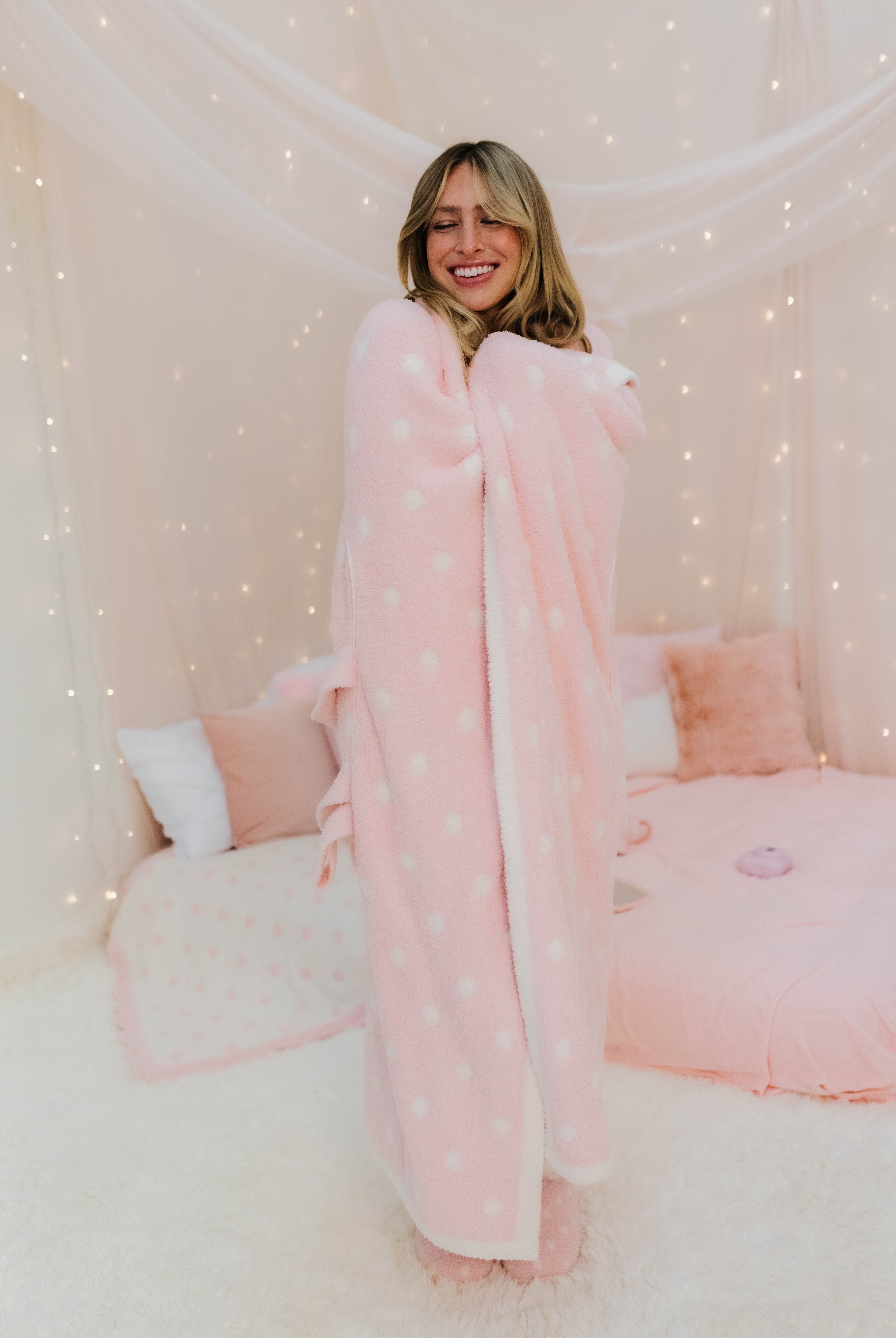 Woman wrapped in a pink polka dot blanket in a cozy room.