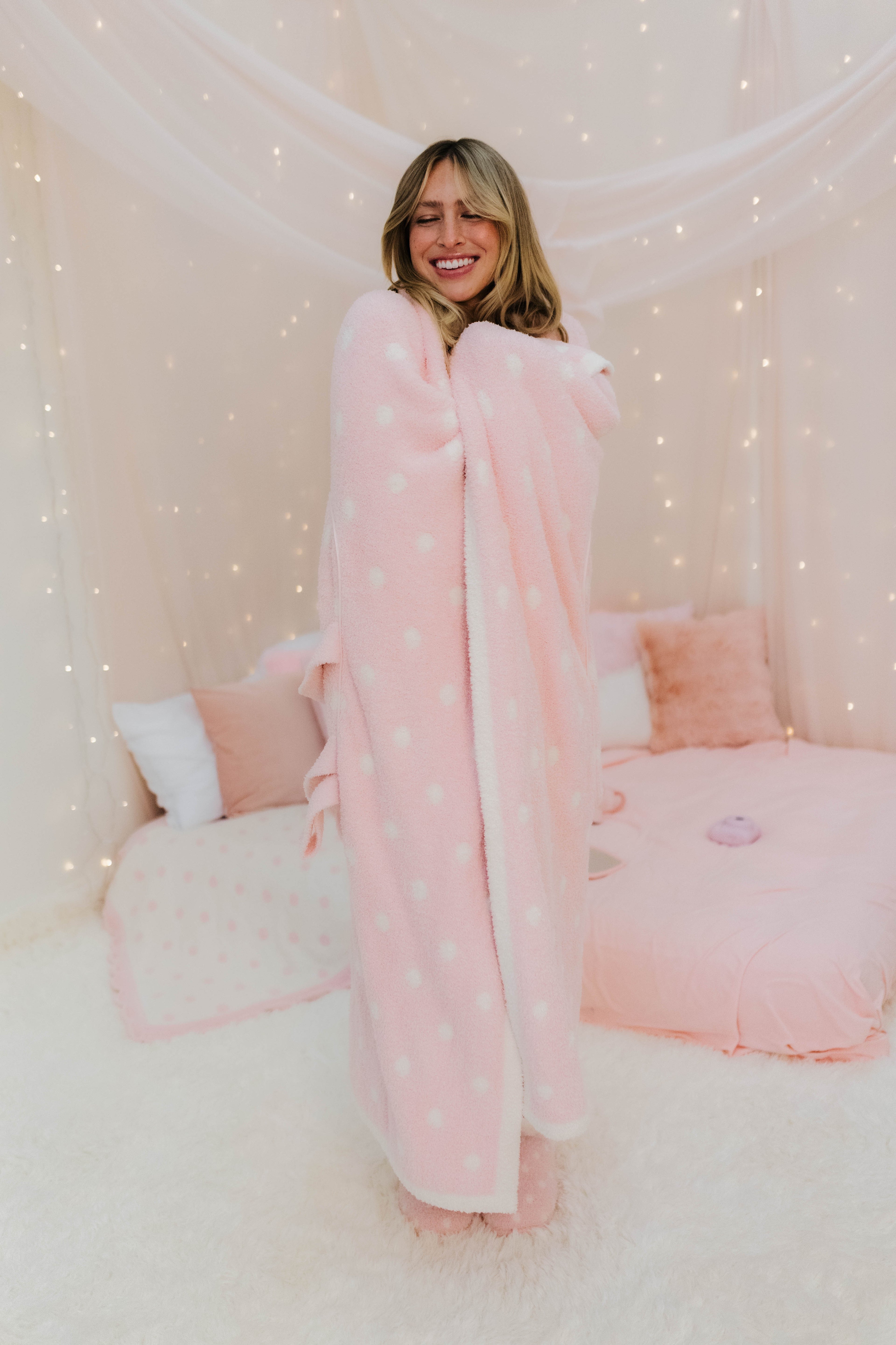 Woman wrapped in a pink polka dot blanket in a cozy room.