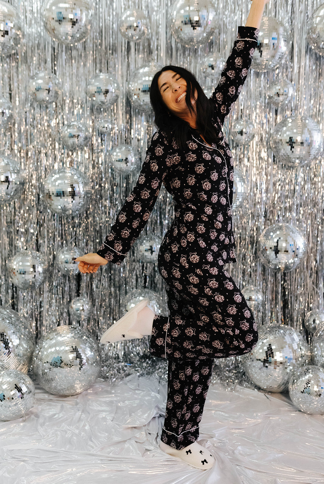 Person in a black patterned outfit posing in front of a silver disco ball curtain.