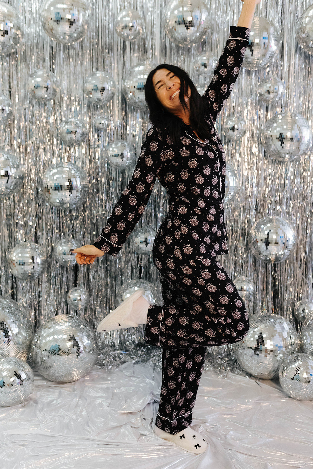 Person in a black patterned outfit posing in front of a silver disco ball curtain.