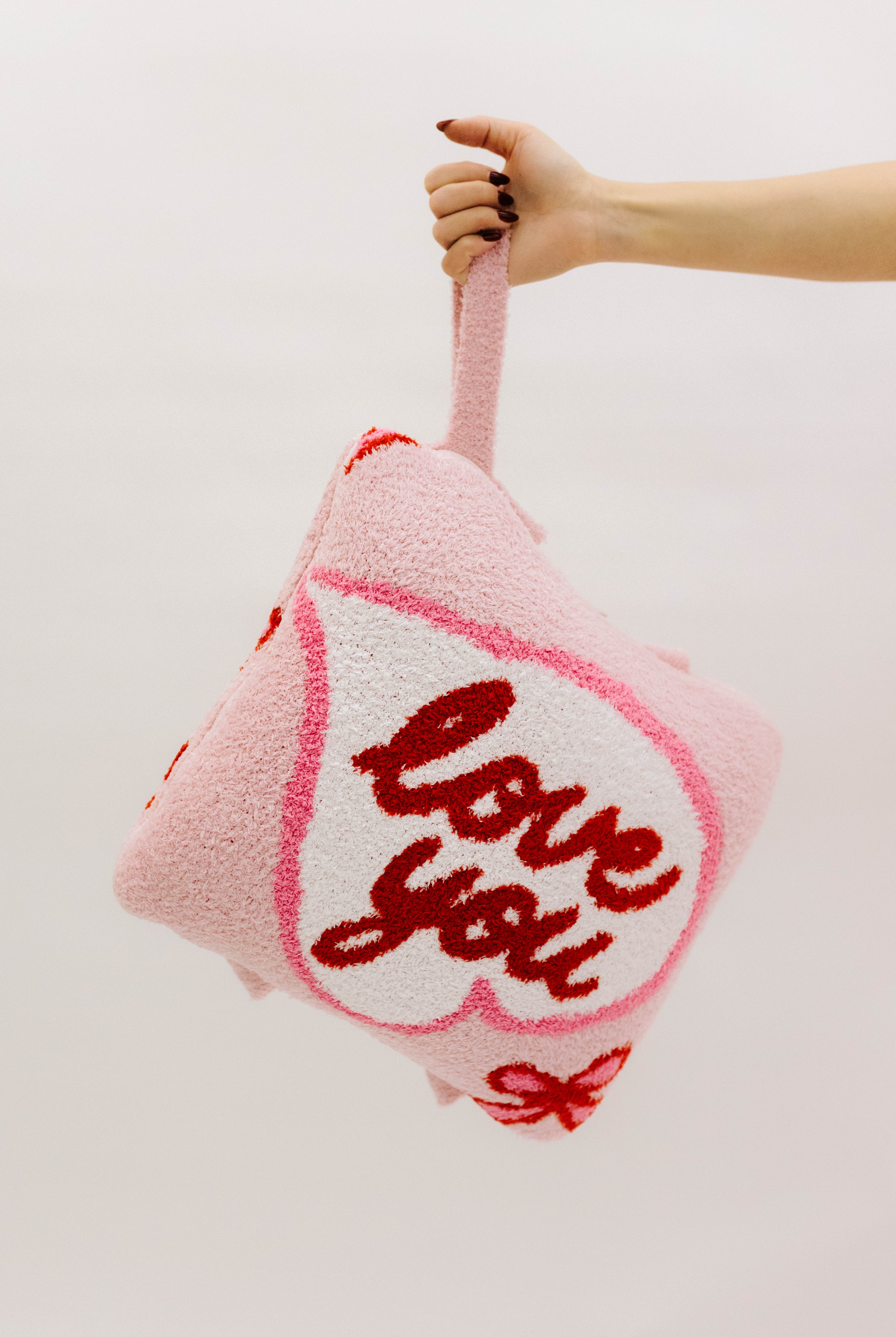Pink pillow with 'love you' text held by a hand against a light background