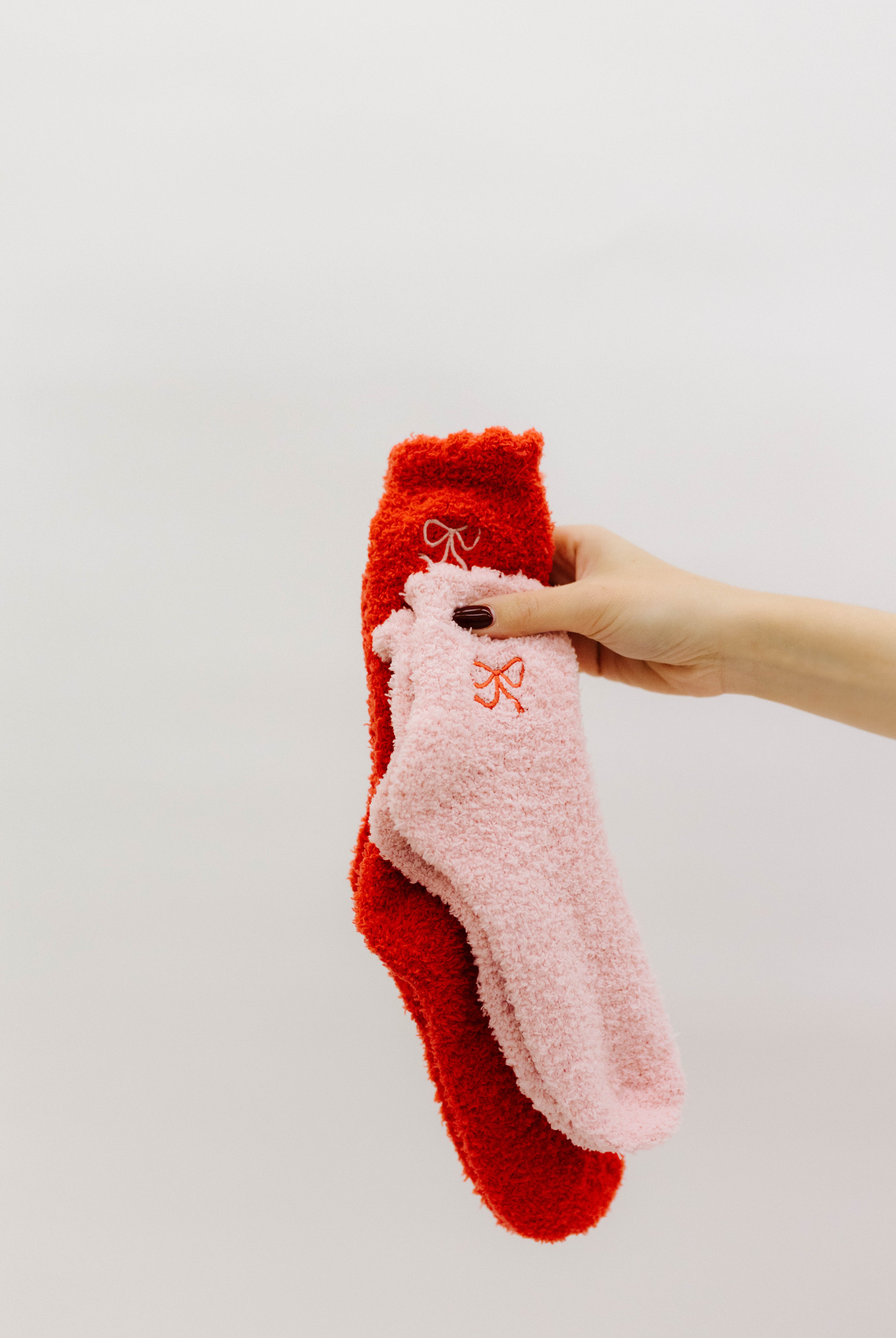 Hand holding two pairs of socks, one red and one pink, against a light background