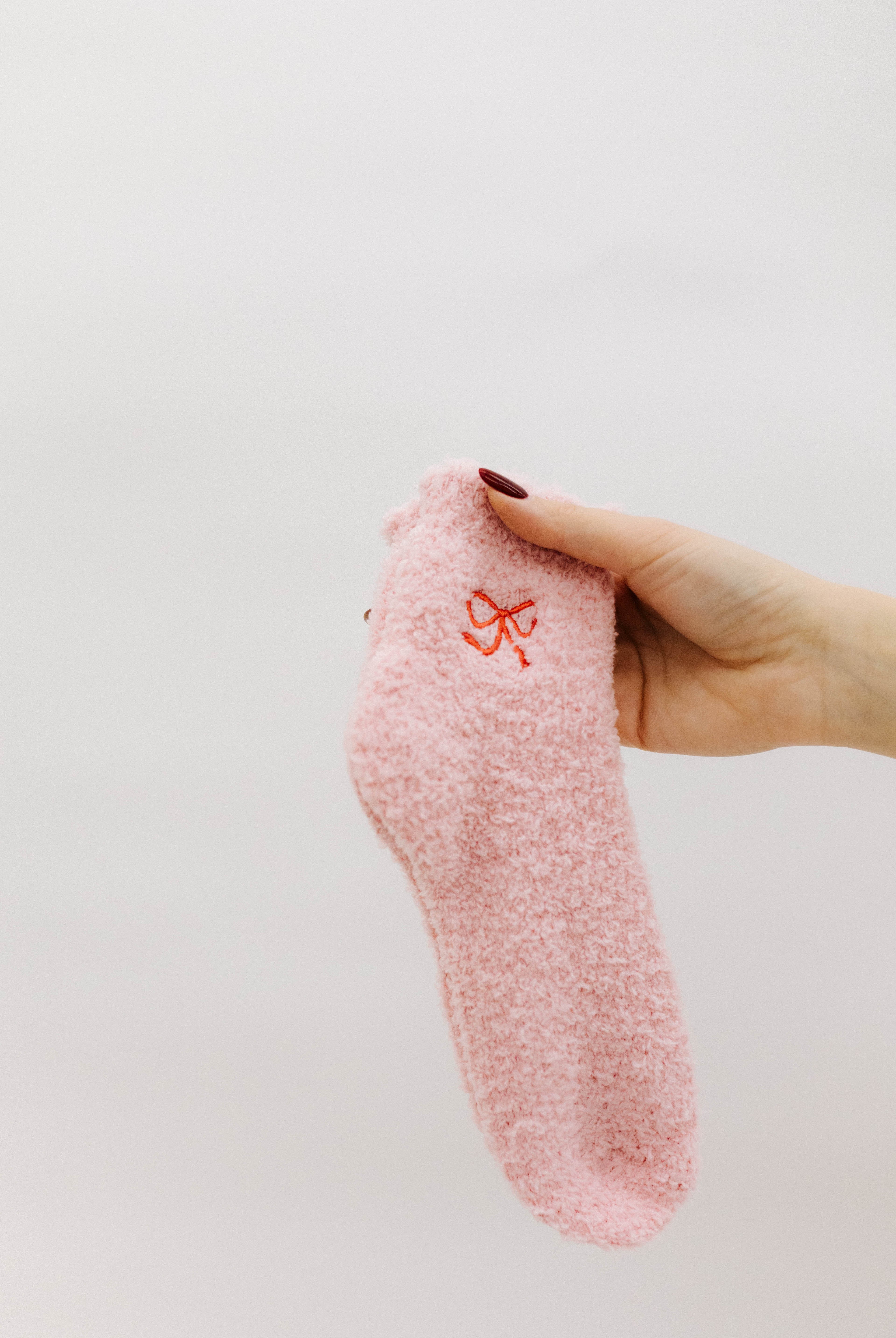 Pink textured sock with a bow print held by a hand against a light background
