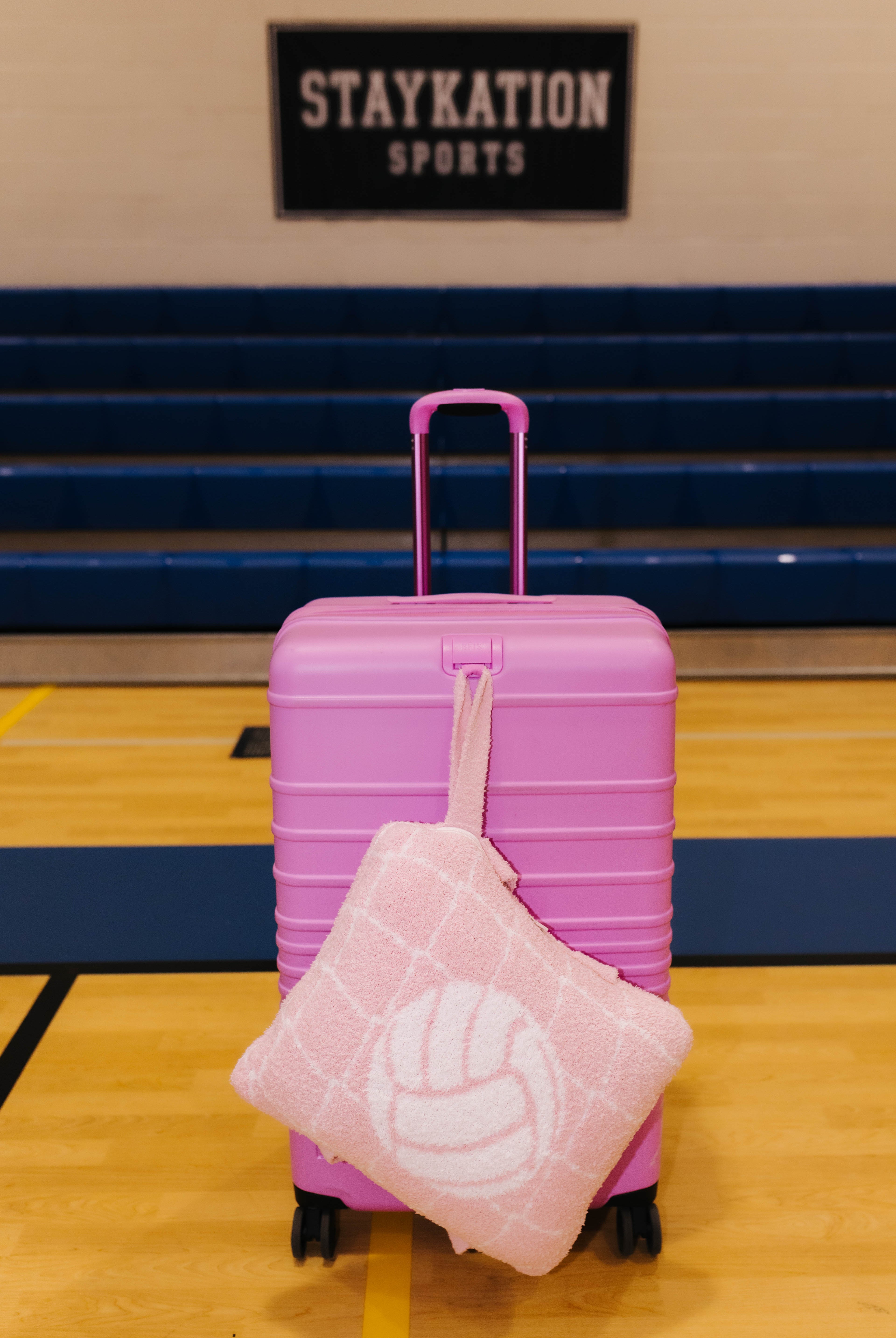 A pink hard-shell suitcase with a volleyball quillow handing off the front of it