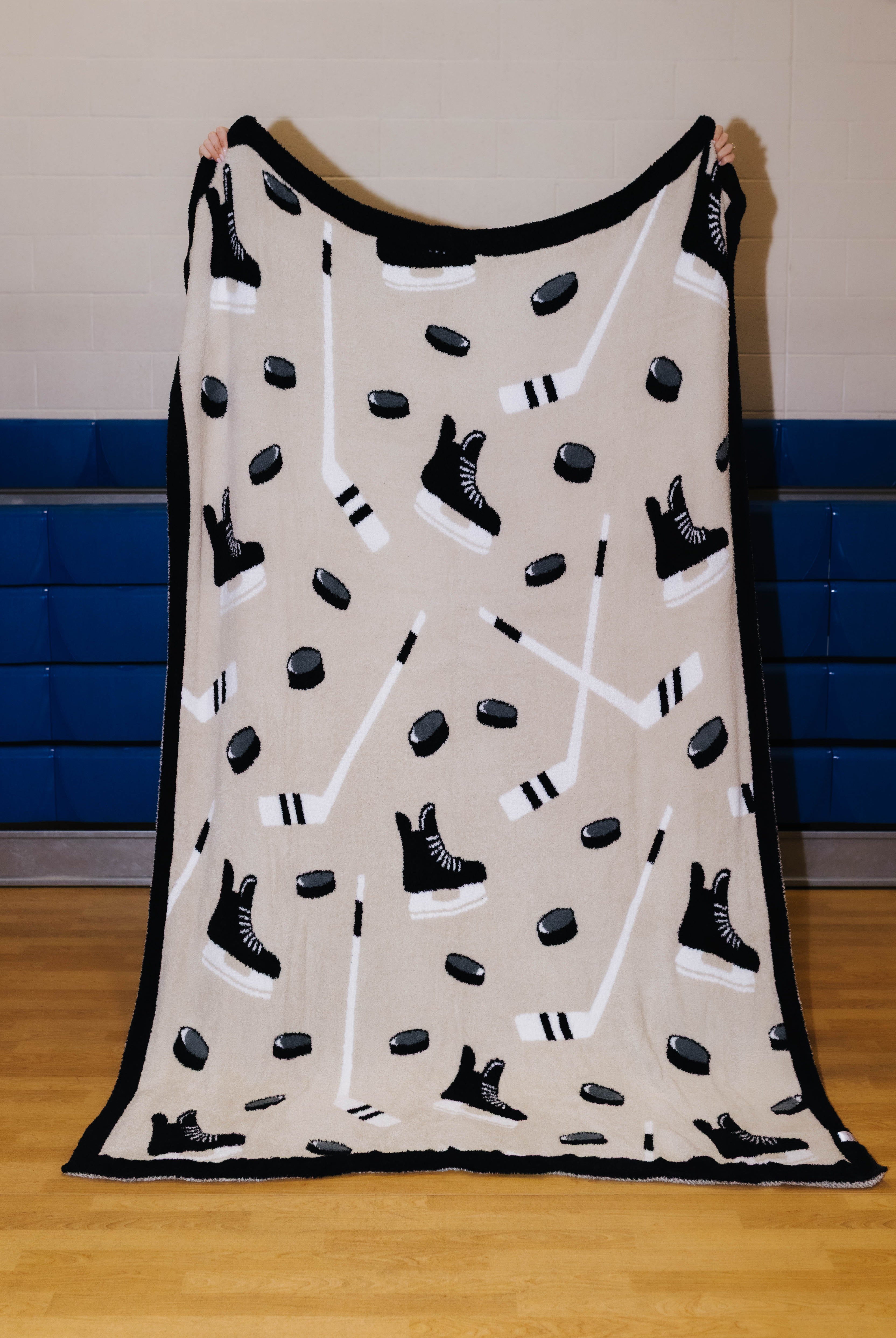 front of hockey blanket being held up showing the black border, skates, sticks, and pucks