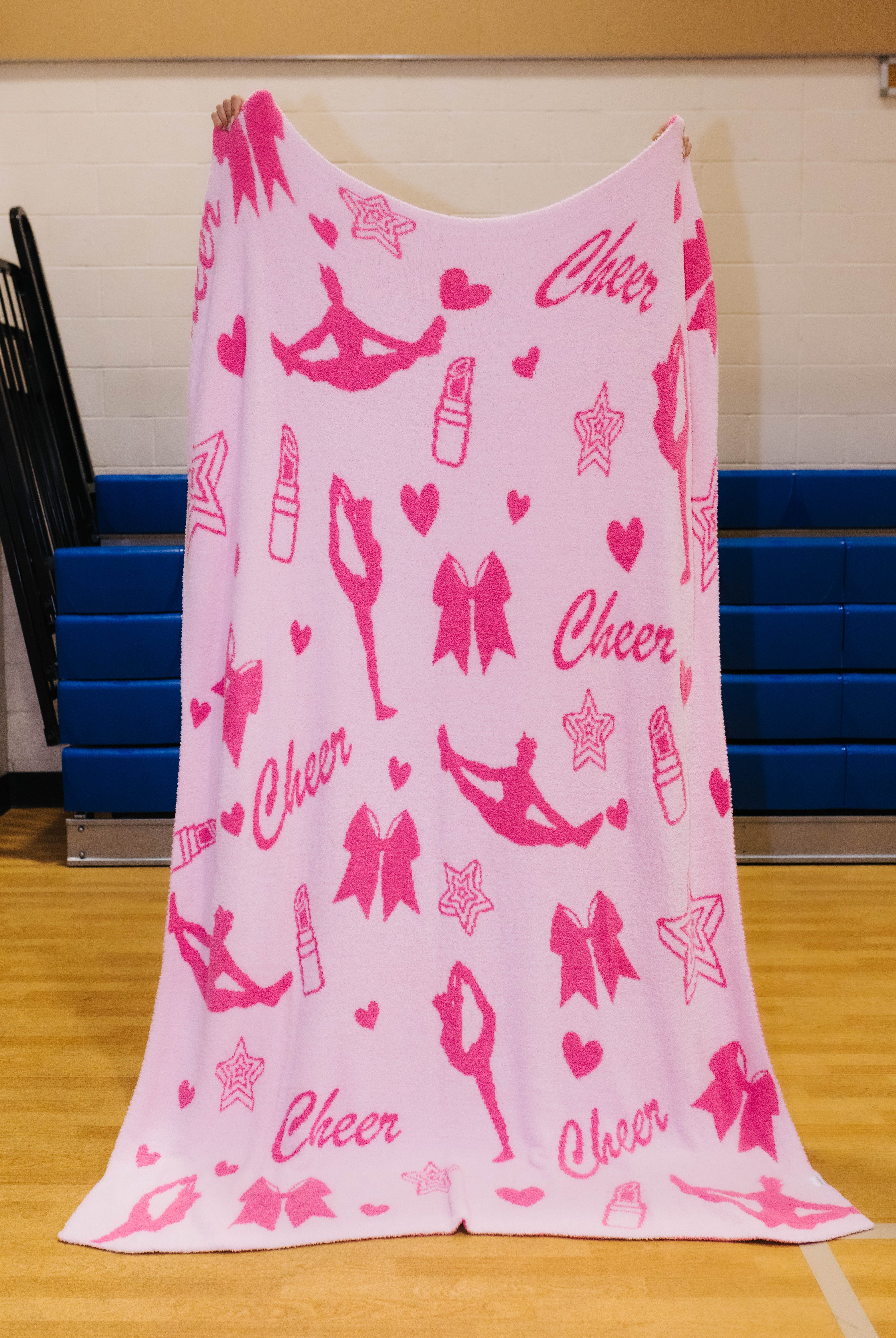 front of cheer blanket showing light pink background and stars, lipstick, hearts, bows, and figures doing stretches/jumps