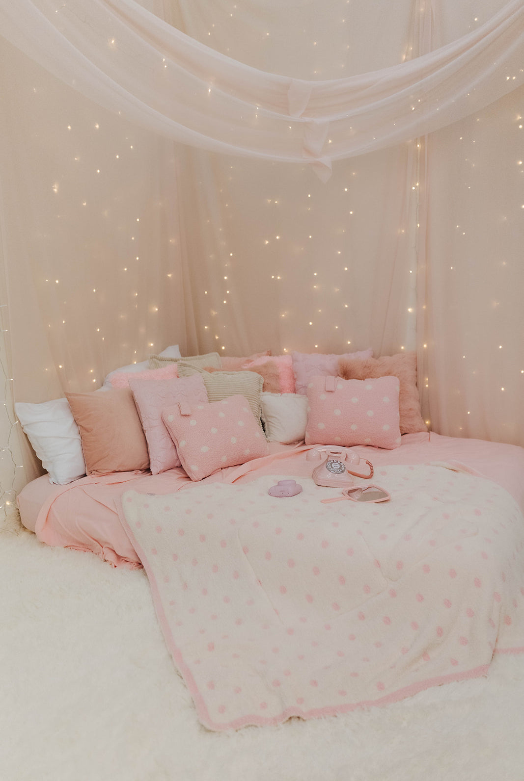 Pink polka dot bedding against a wall with fairy lights
