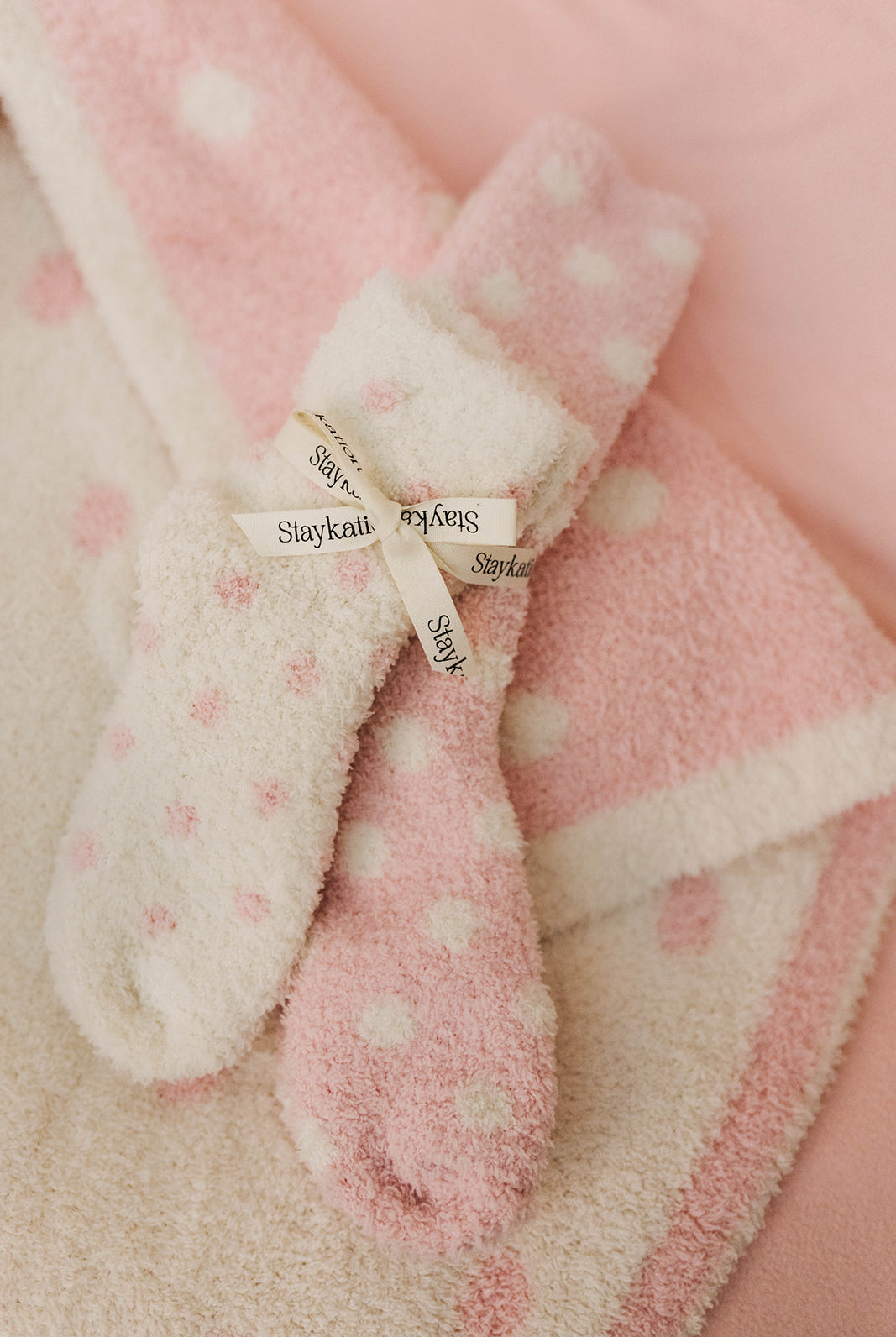 Pink and white polka dot socks with 'Staykation' label on a pink background