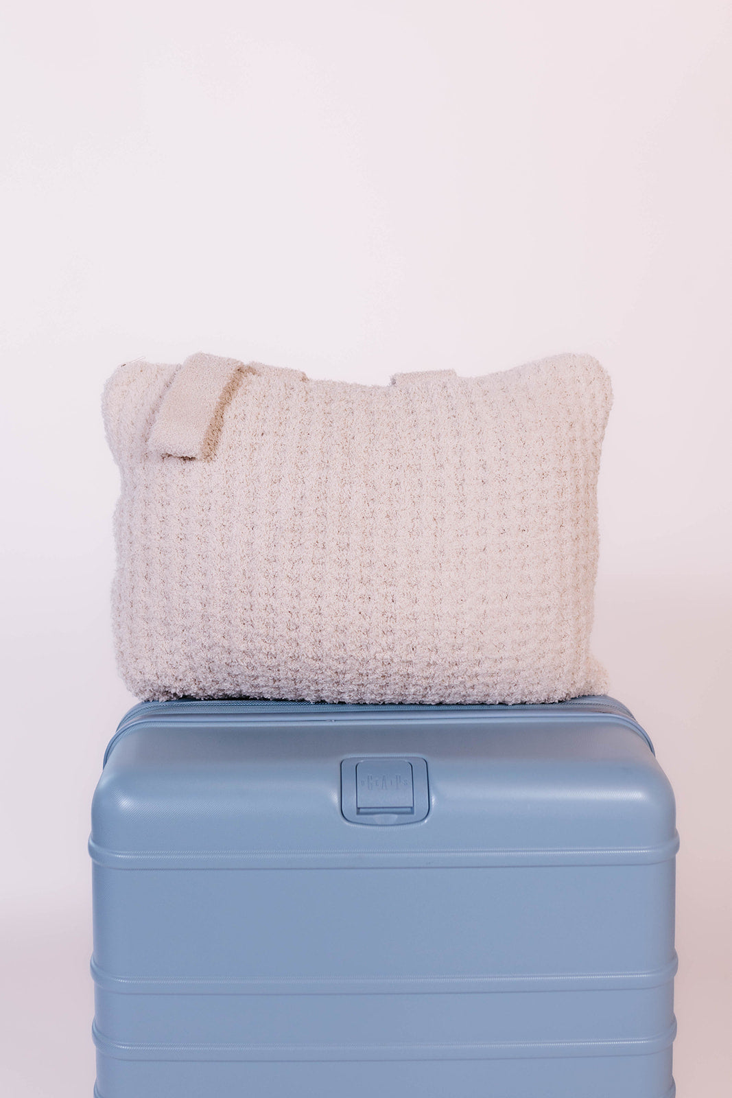 Textured beige quillow on a blue suitcase against a white background