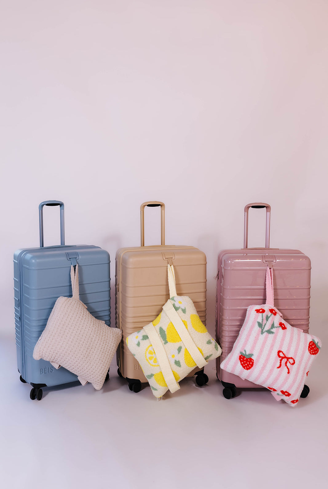 Three suitcases of different colors with matching quillows on a light background