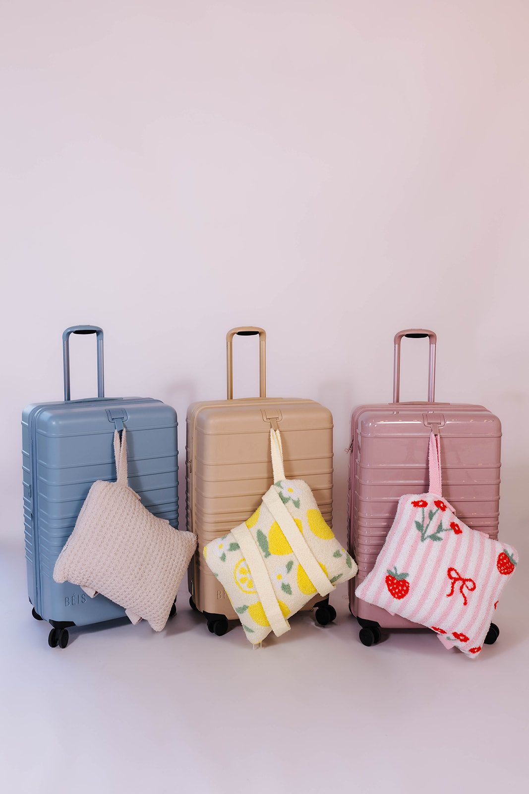 Three suitcases of different colors with matching quillows on a light background