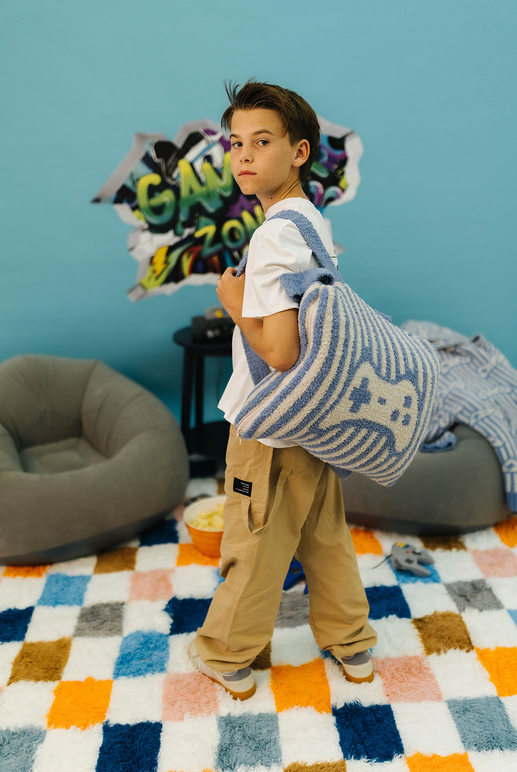 Child holding a striped gaming quillow in a room with colorful rug and blue wall