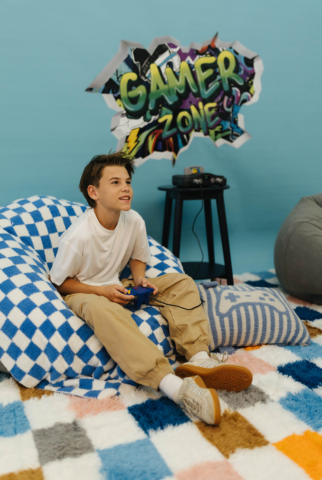 Young boy sitting on a bean bag chair in a room with 'Gamer Zone' decor.