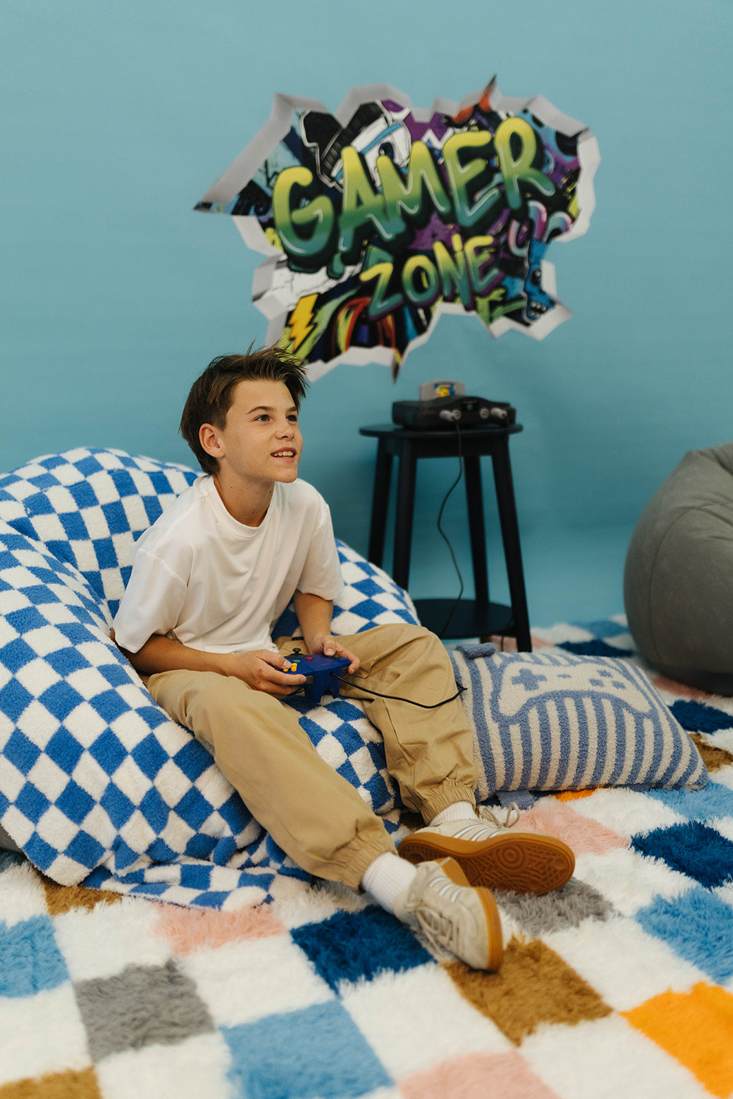 Young boy sitting on a bean bag chair in a room with 'Gamer Zone' decor.