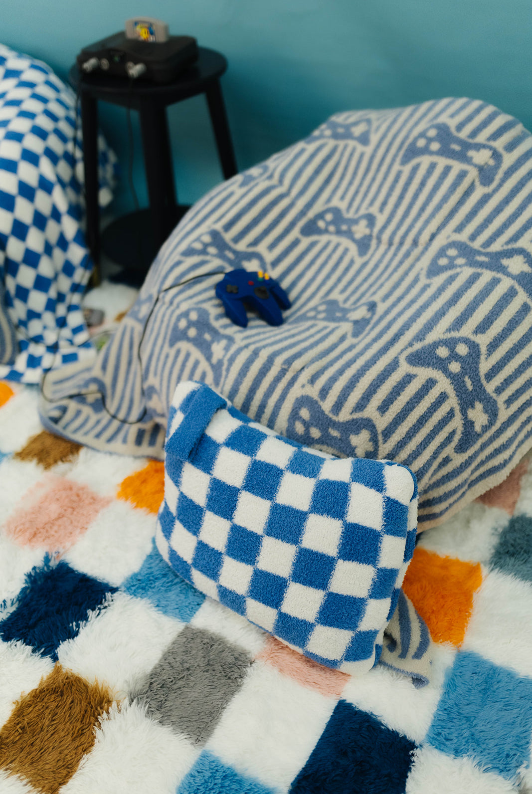 Blue and white checkered pillow on a colorful blanket with a blue wall background