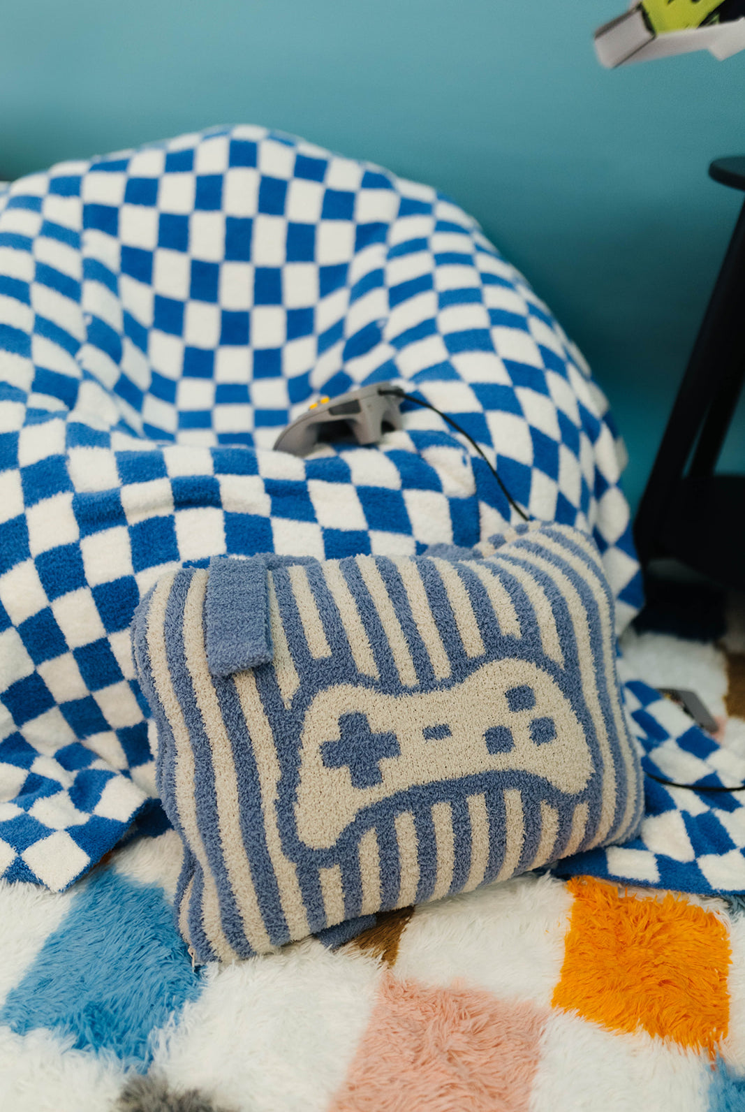 Blue and white checkered bean bag chair with a striped pillow featuring a game controller design on a colorful rug.