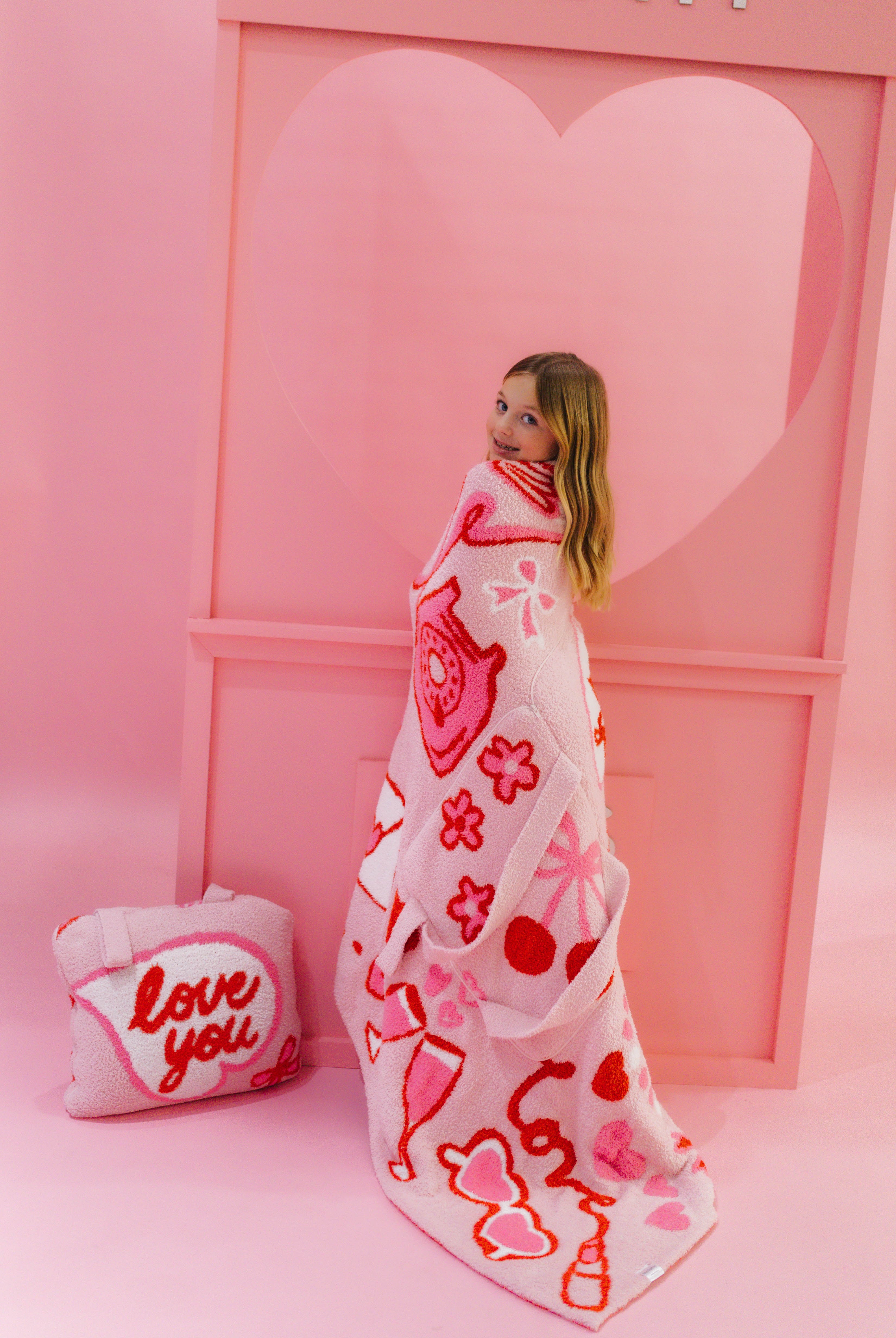 Person wrapped in a heart-patterned blanket with a pink heart-shaped door in the background