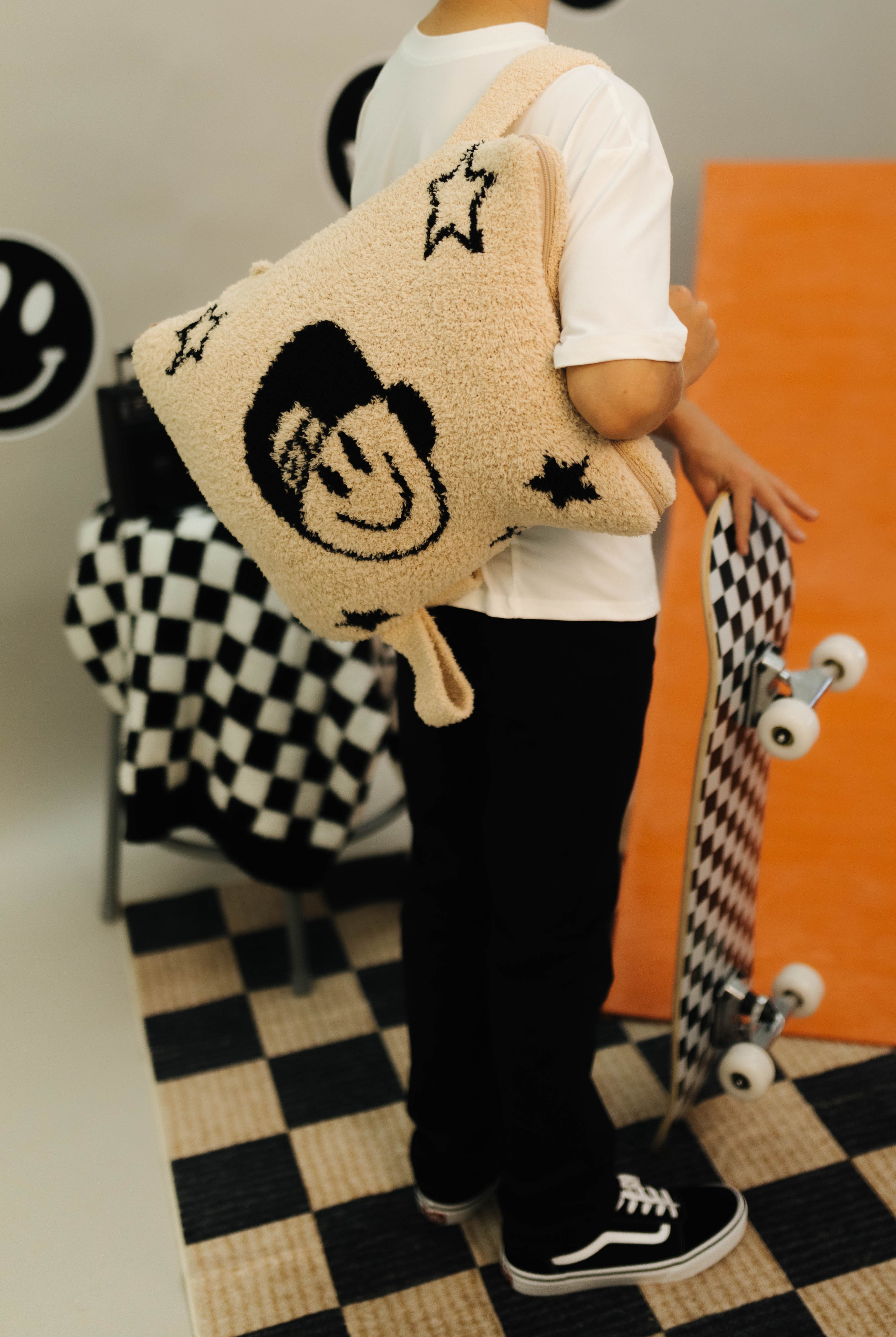 Person holding a quillow with star and smiley face patterns on a checkered floor.