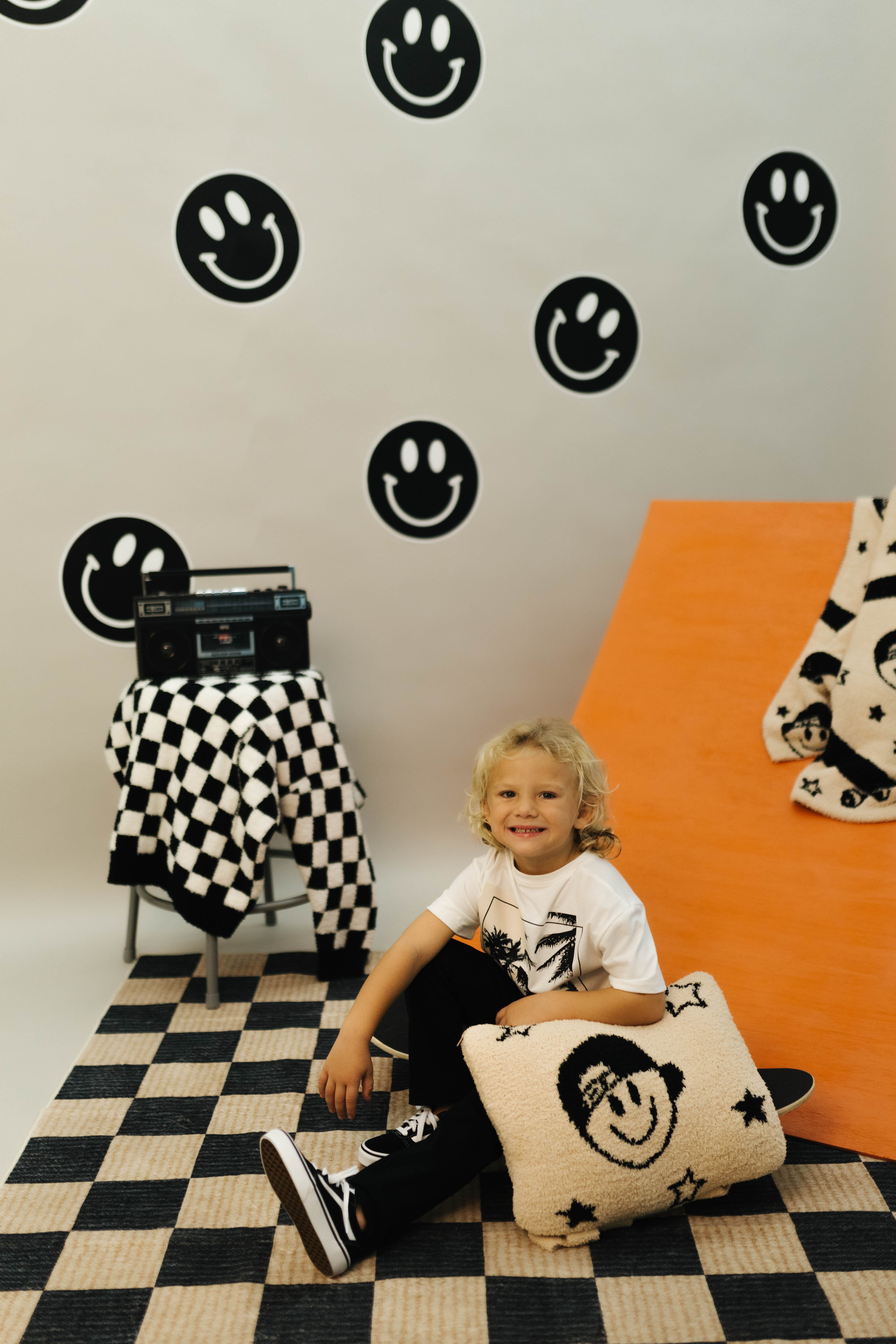 Child sitting on a checkered floor with smiley face decorations on the wall and floor.