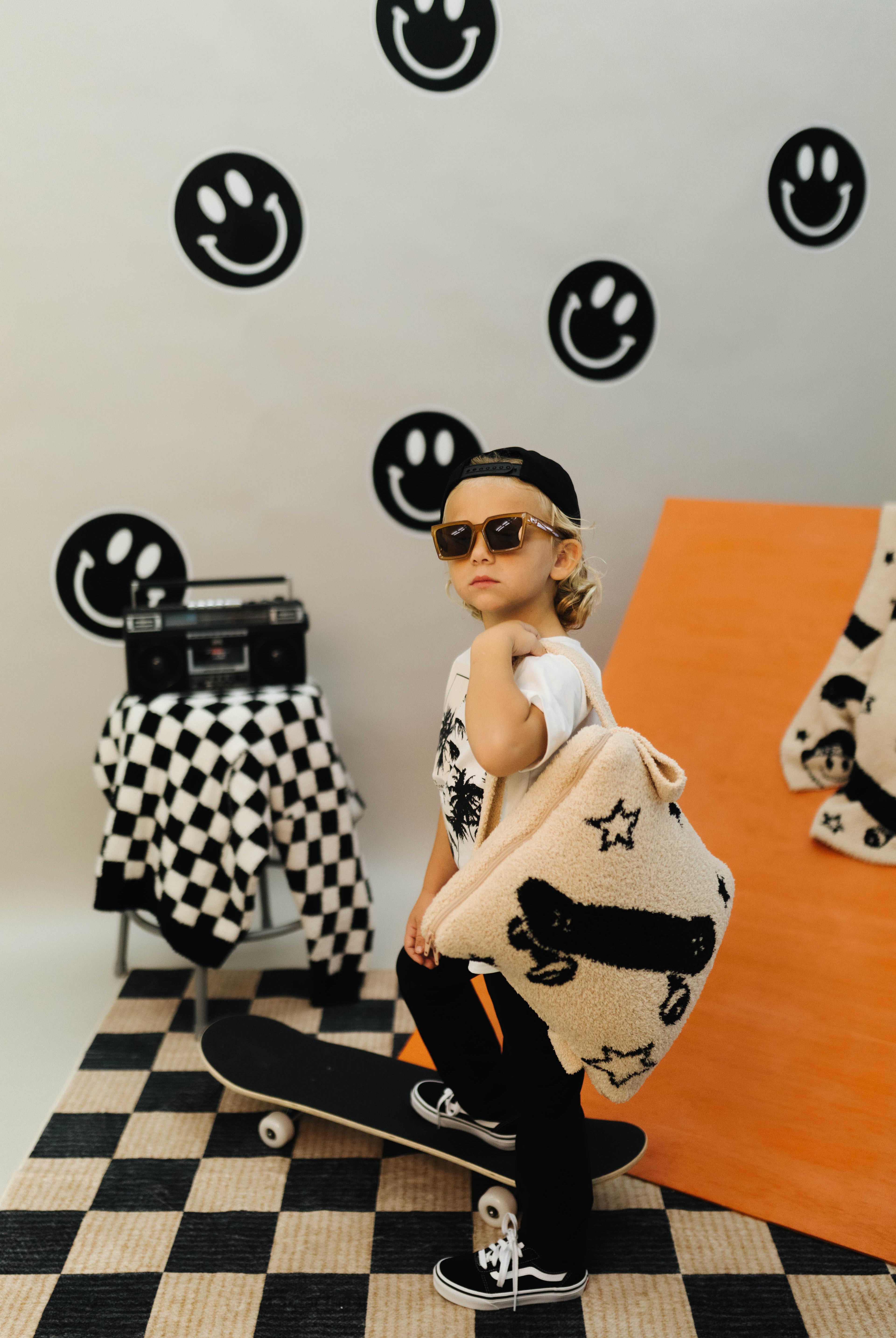 Person holding a patterned quillow in a room with checkered floor and smiley face wall decorations