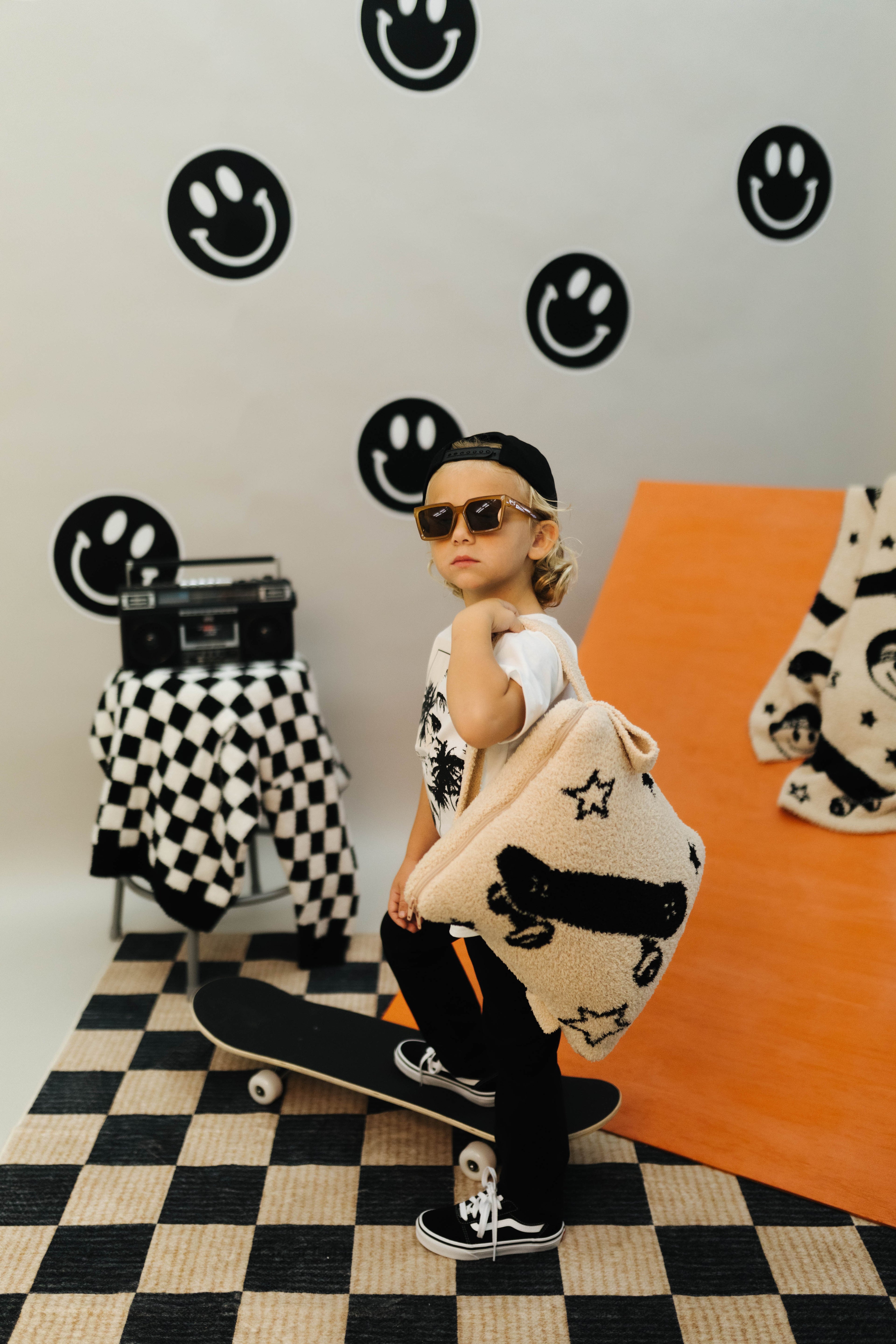 Person holding a patterned quillow in a room with checkered floor and smiley face wall decorations