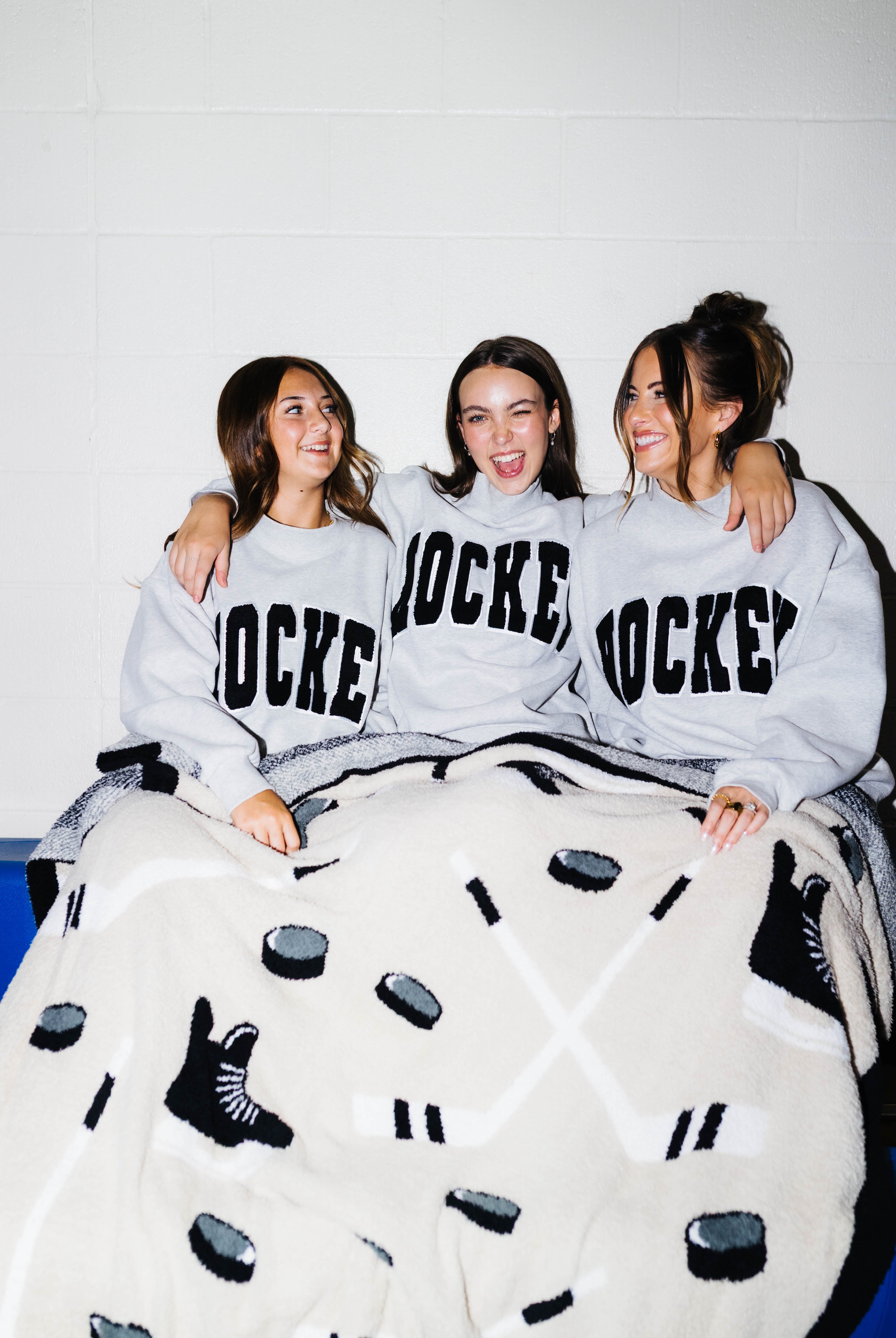 Three girls sitting on bleachers smiling with the hockey blanket on them