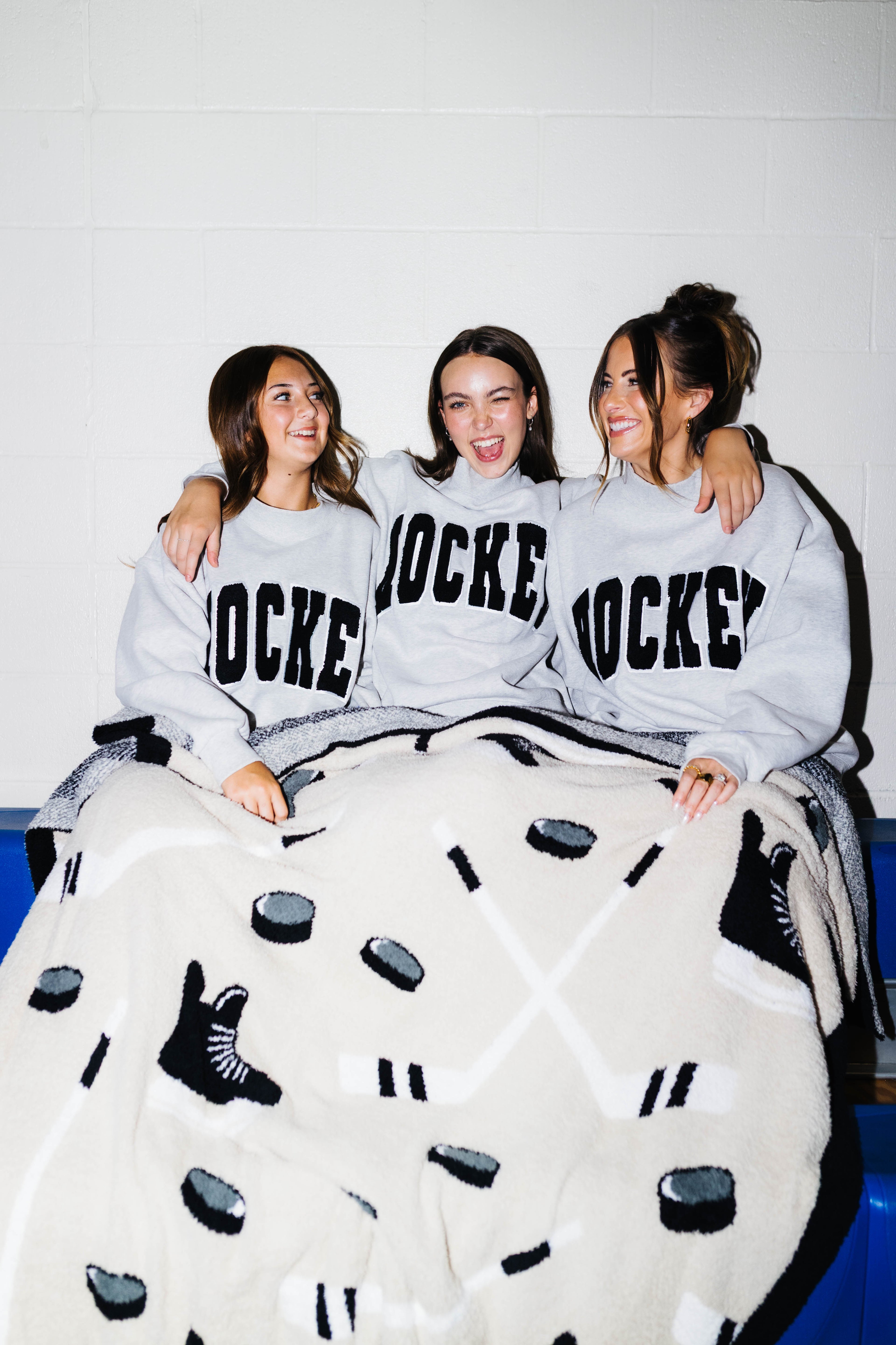 Three girls sitting on bleachers smiling with the hockey blanket on them