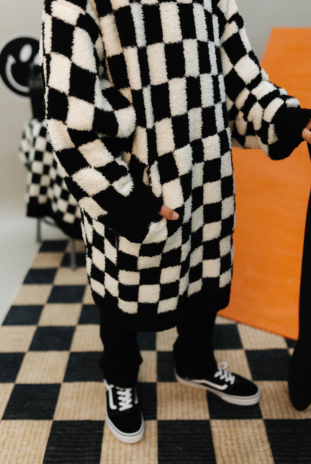 Person wearing a black and white checkered wearable with sneakers on a checkered floor.