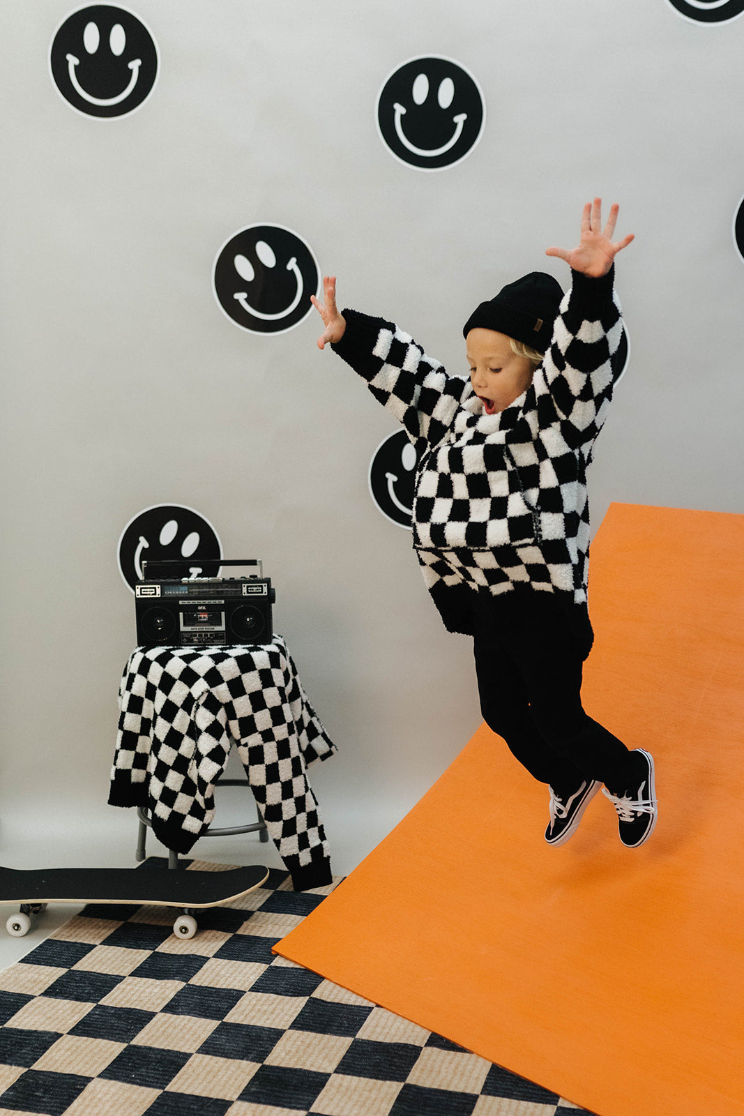 Person in a checkered wearable jumping on an orange mat with smiley face decorations on the wall.