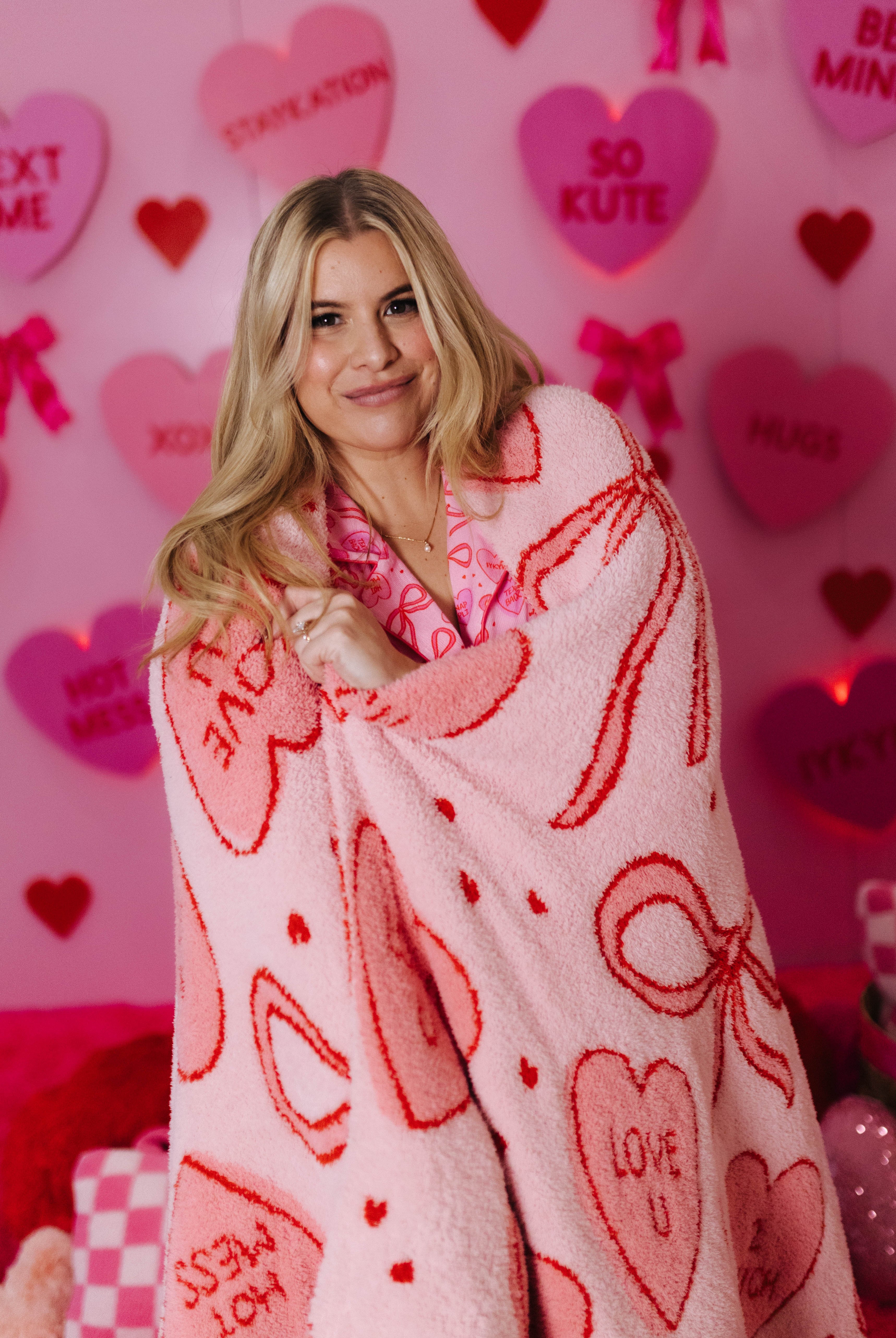 Woman wrapped in a heart-patterned blanket against a pink background with hearts and text.