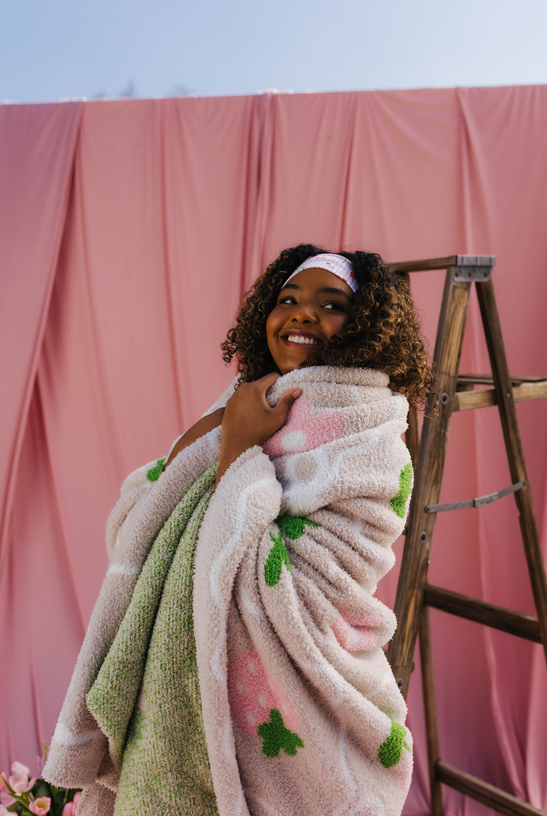 Woman wrapped in a blanket with pink and green patterns against a pink backdrop